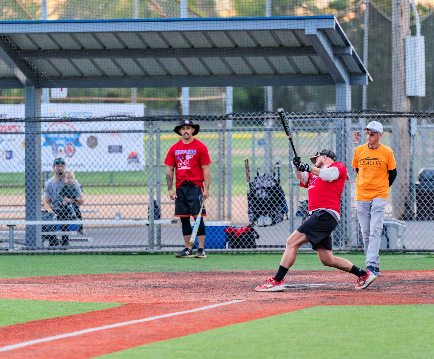 Batter swings at a pitch during a casual softball game on an outdoor field.
