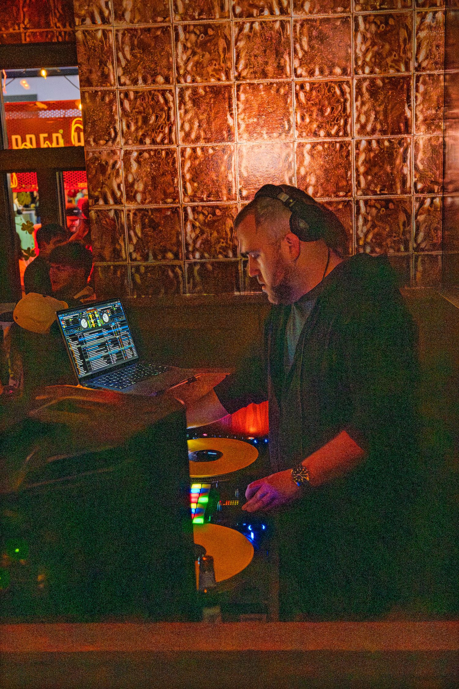 DJ mixing music on turntables with laptop at a dimly lit nightclub event venue.