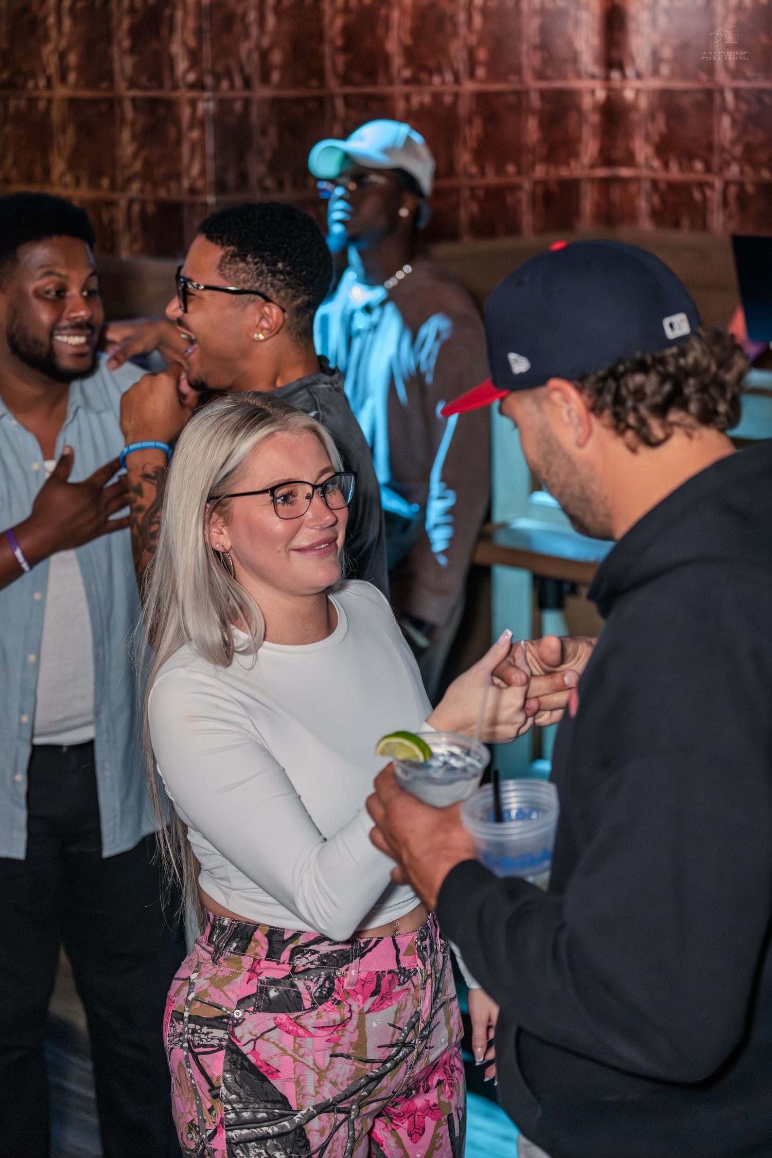 Smiling blonde woman in white top interacting with a man holding a cocktail at a party.