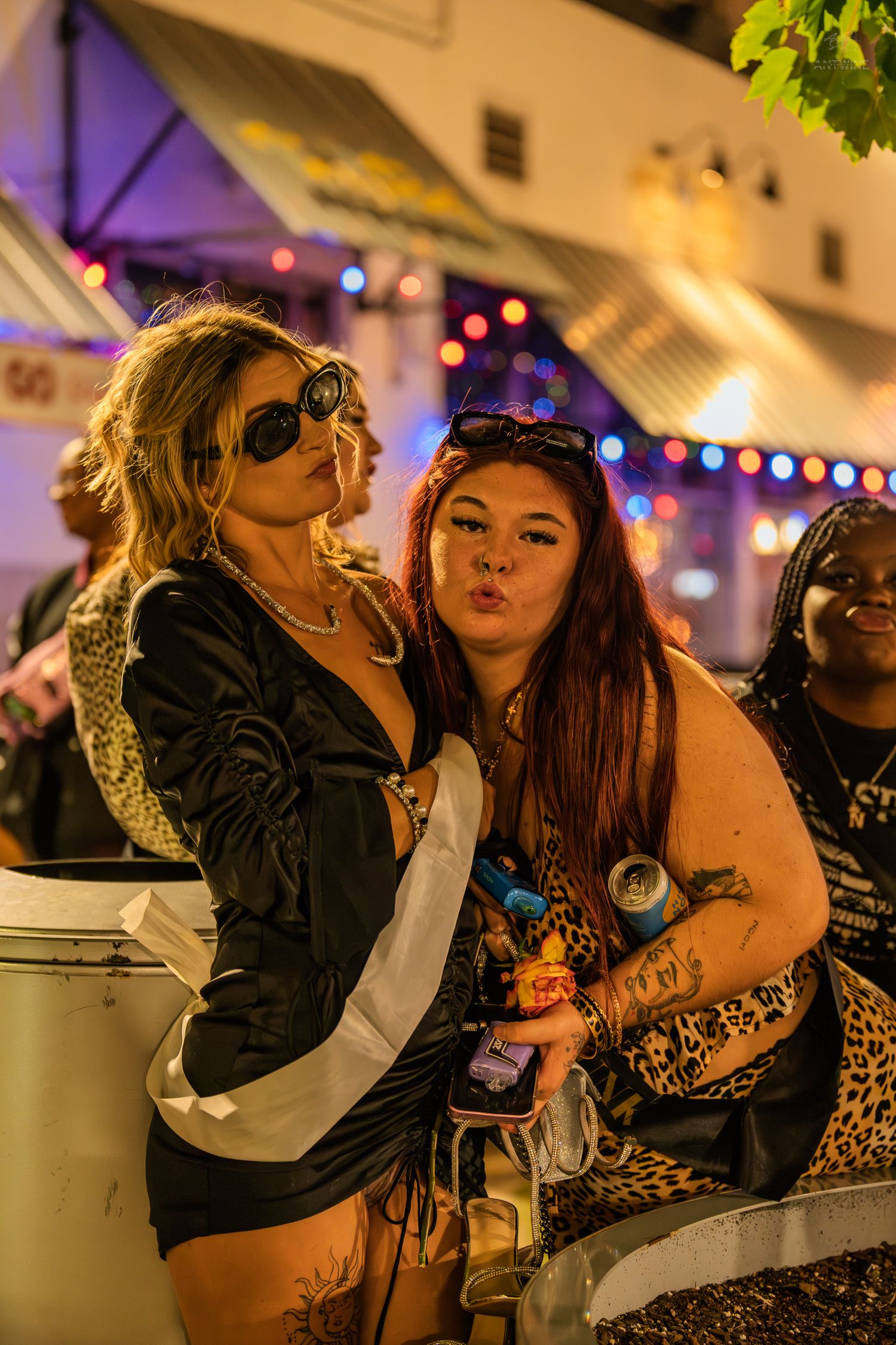 Two women posing together at an outdoor nighttime festival with colorful lights.