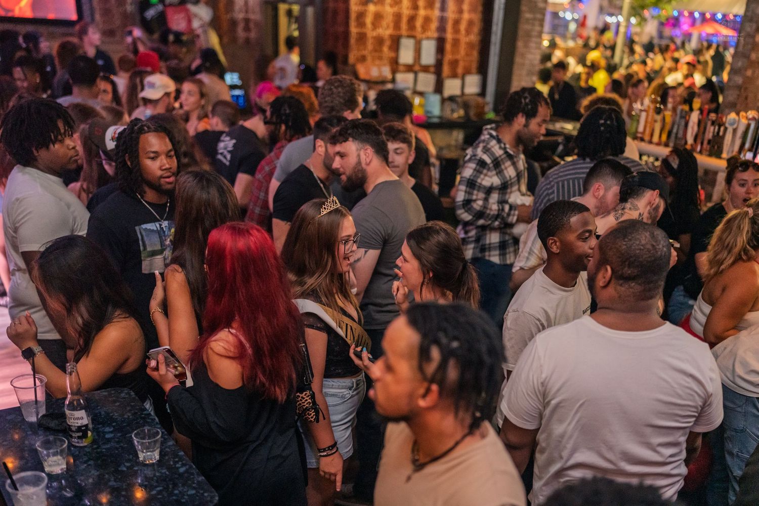 Diverse group of partygoers socializing and dancing at a lively nightclub with warm lighting.