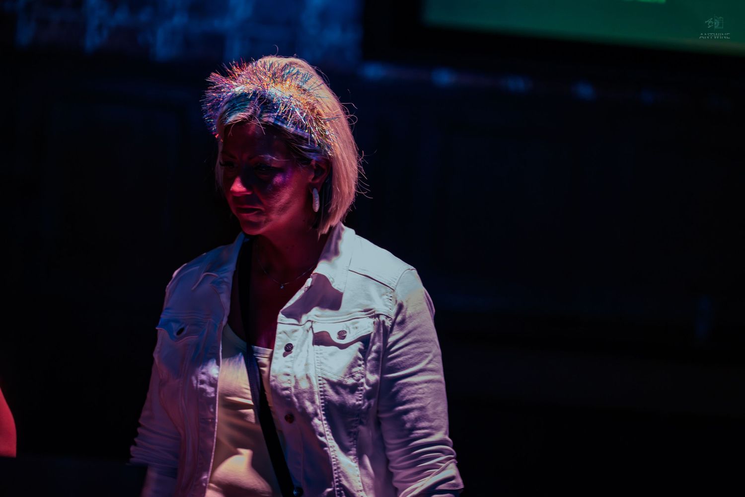 Woman in white denim jacket standing under dramatic stage lighting at event.