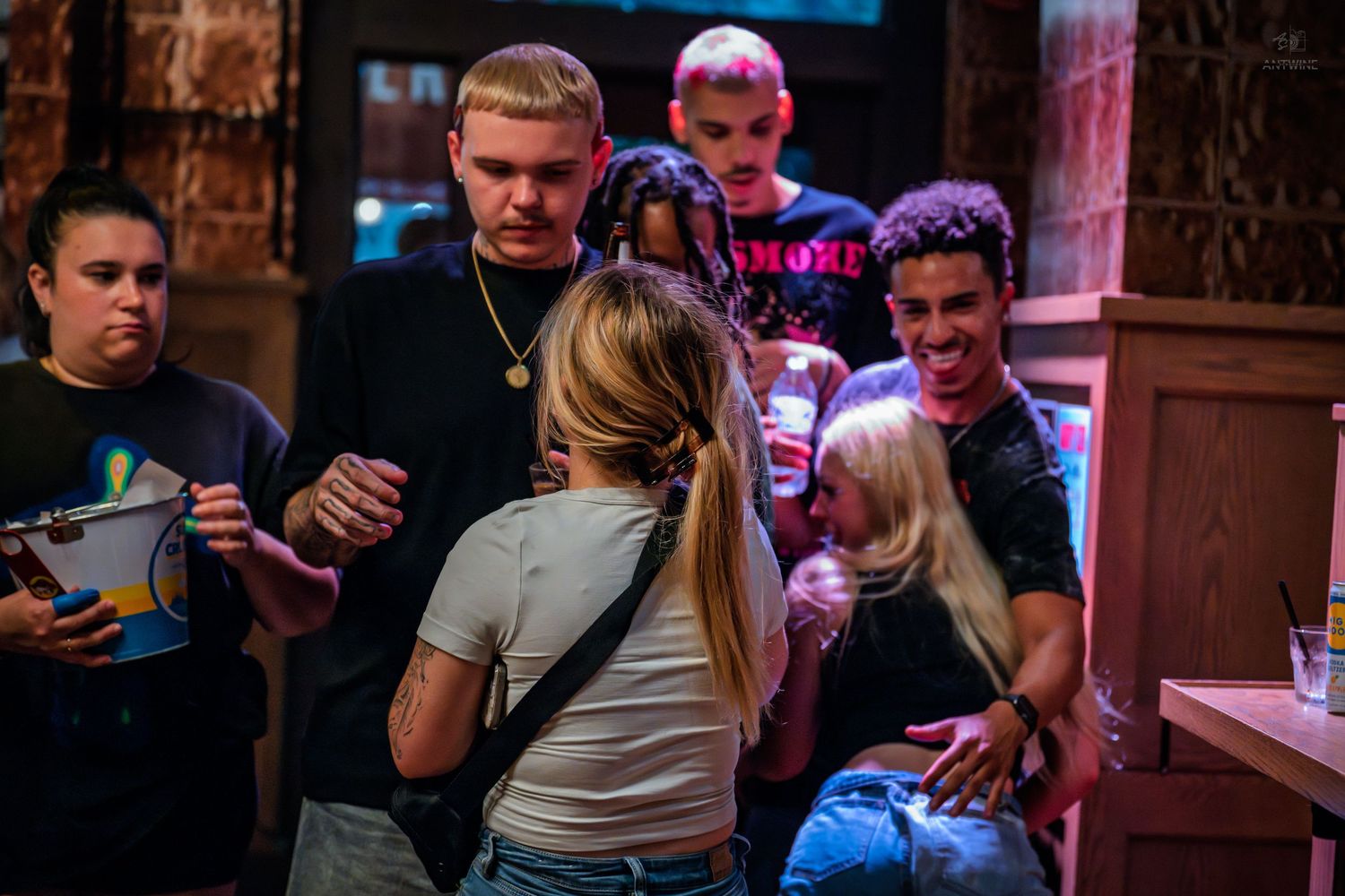 Group of young people mingling and chatting inside a dimly lit bar or nightclub.