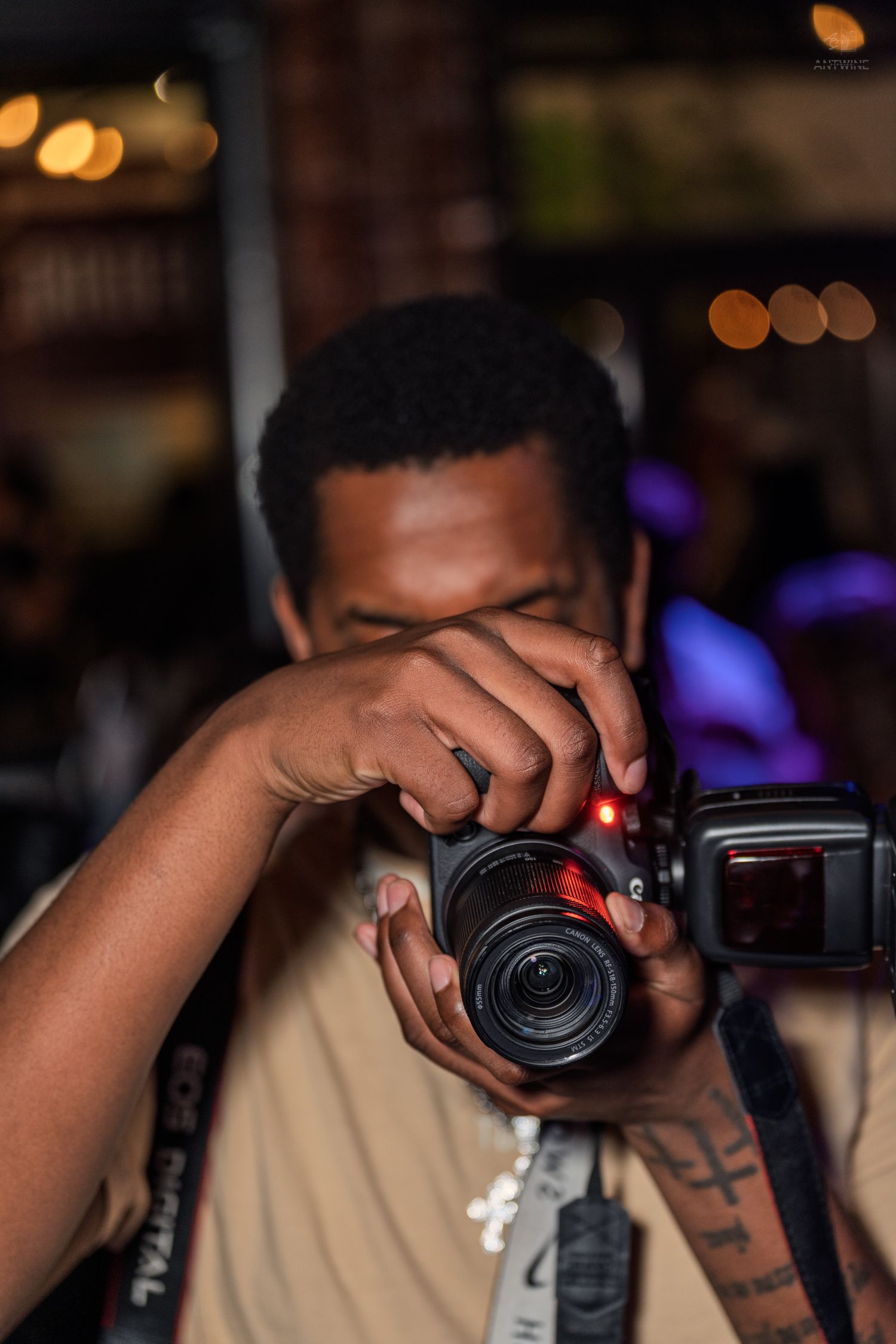 Close-up of a photographer adjusting a Canon DSLR camera at a dimly lit nightlife event.