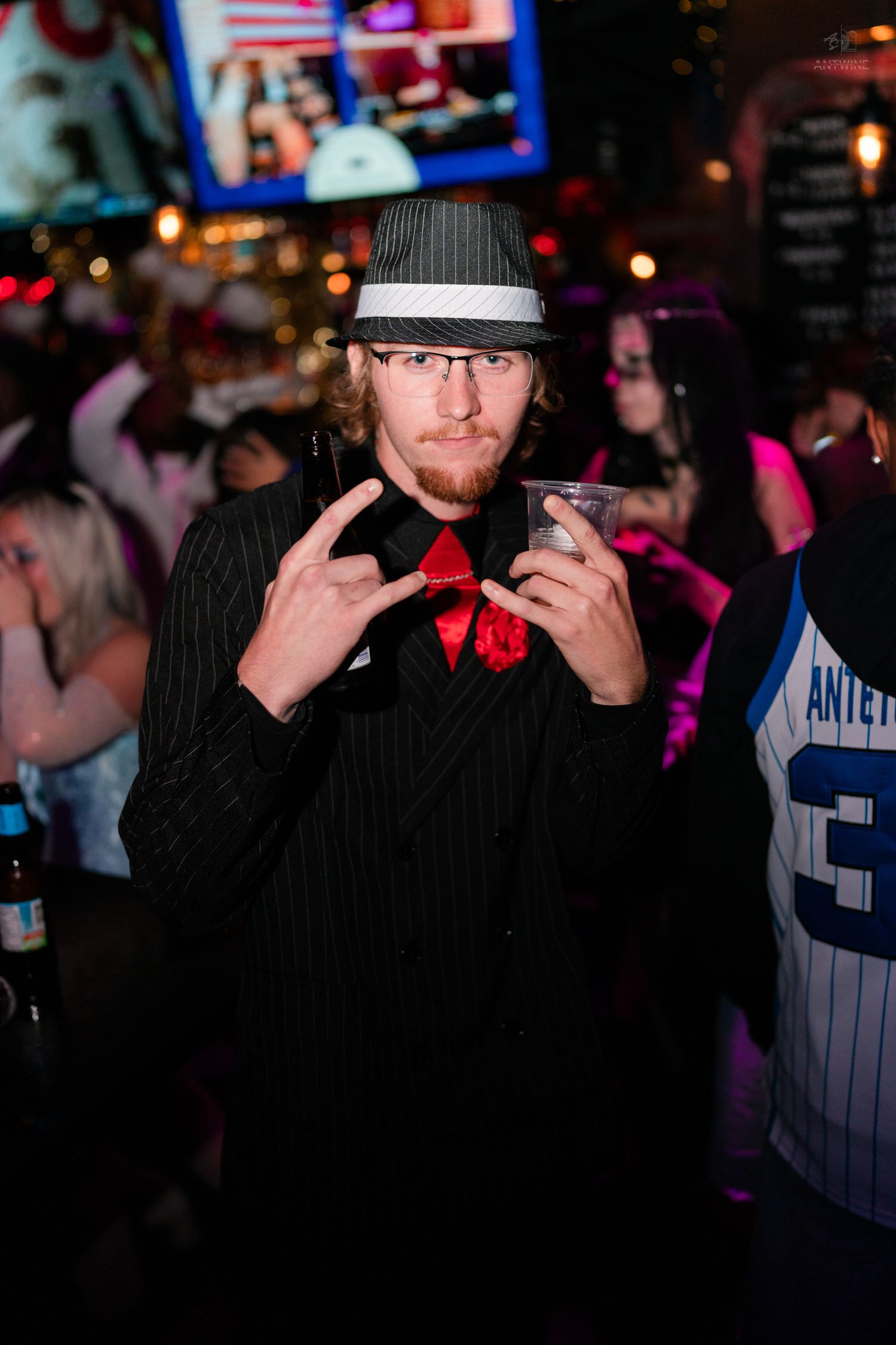 Man in pinstripe suit and fedora Halloween costume posing with a drink at a party.