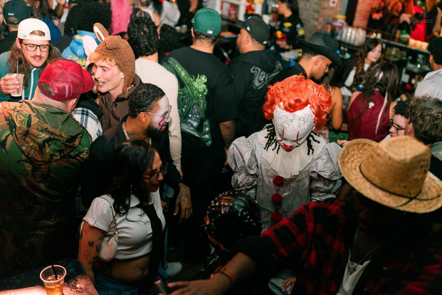 Packed Halloween party with guests in costumes including a Pennywise clown in a lively bar setting.