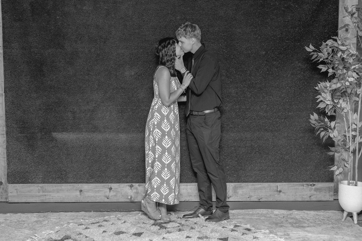 Black and white photo of a couple sharing a romantic kiss at a wedding reception near a dark backdrop.