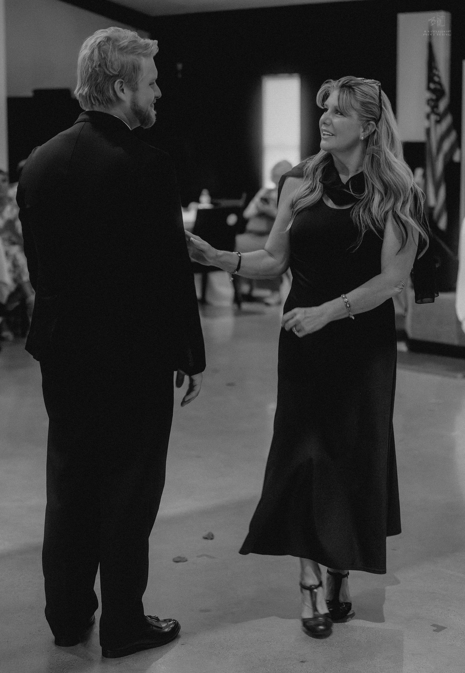 Elegant couple in black attire sharing a conversation on a dance floor at a formal event.