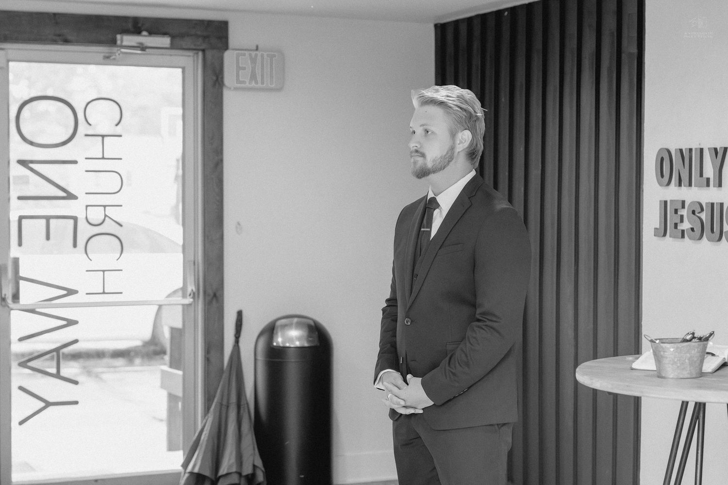 Man in suit standing in black and white church interior with One Way and Only Jesus signs visible.