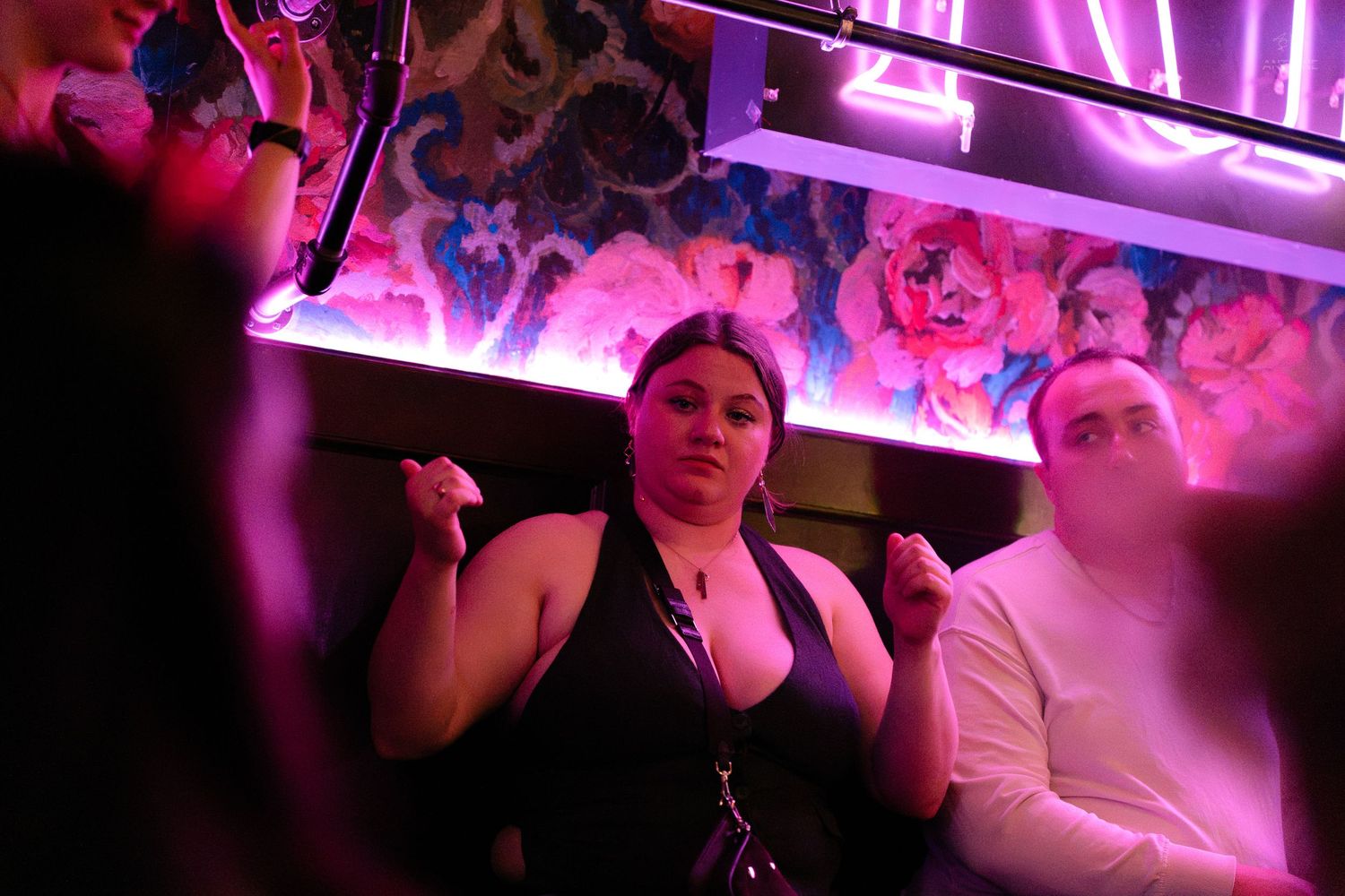 Woman dancing confidently at a nightclub with purple neon lights and floral wallpaper background.