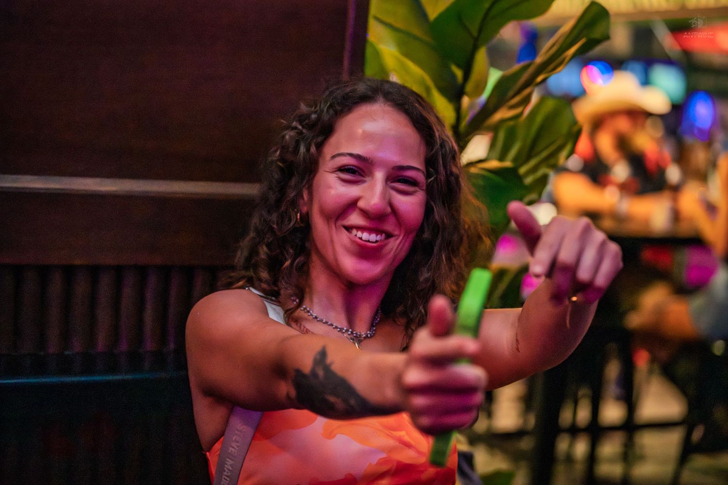 Smiling woman with tattoos points at camera during a tropical-themed bar event.