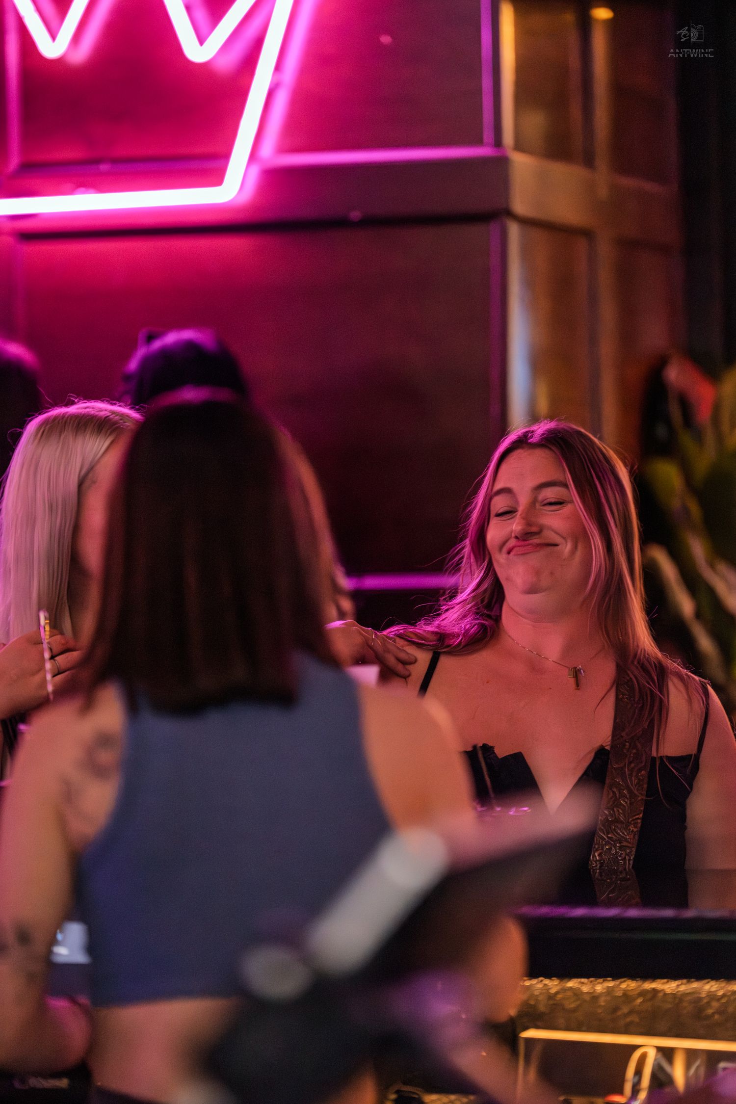 Woman smiling and socializing with friends at a bar under pink neon lights.