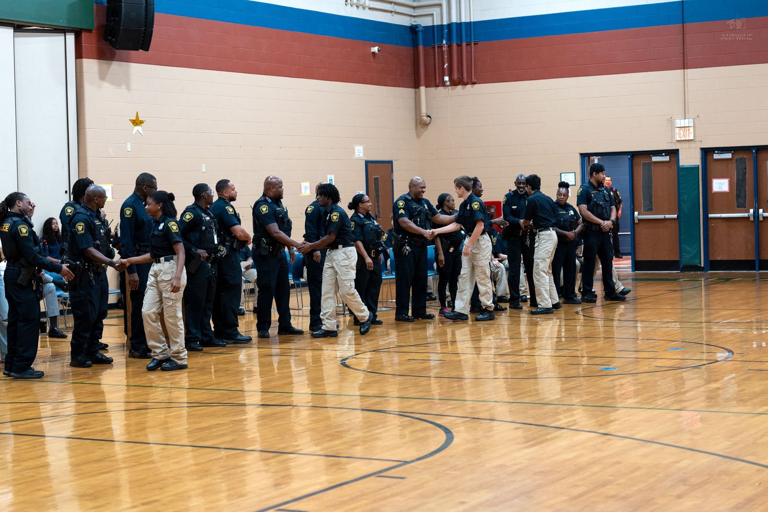 Group of police officers in uniform standing in a line inside a school gymnasium.
