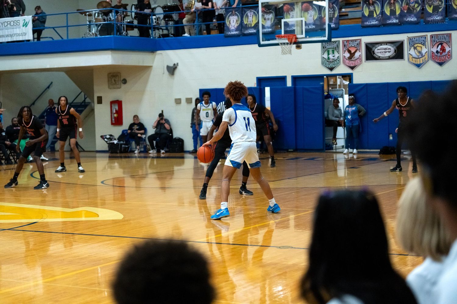 Player #11 in blue dribbles basketball during high school game.