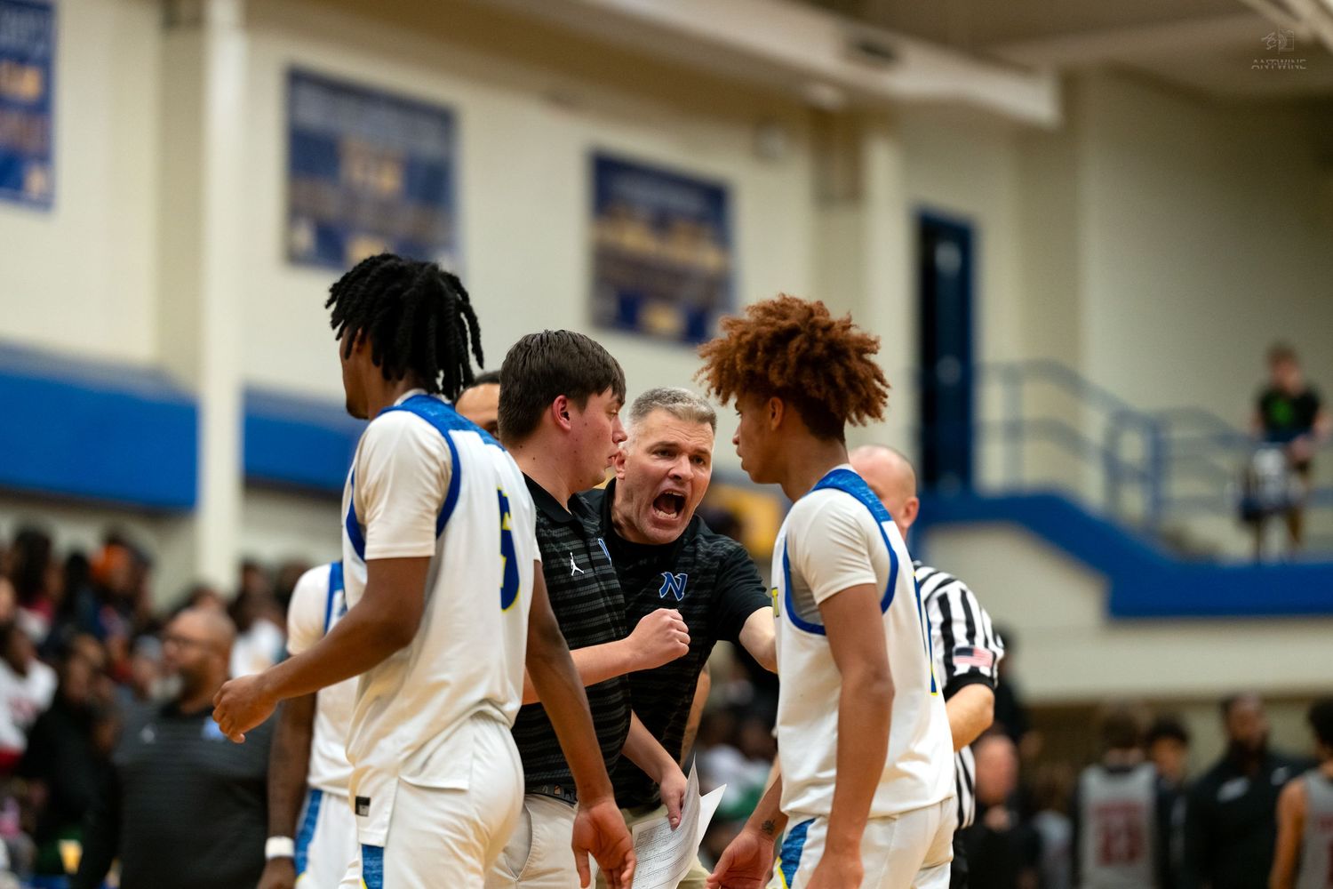 A coach energetically motivates his players during a huddle at a high school basketball game.