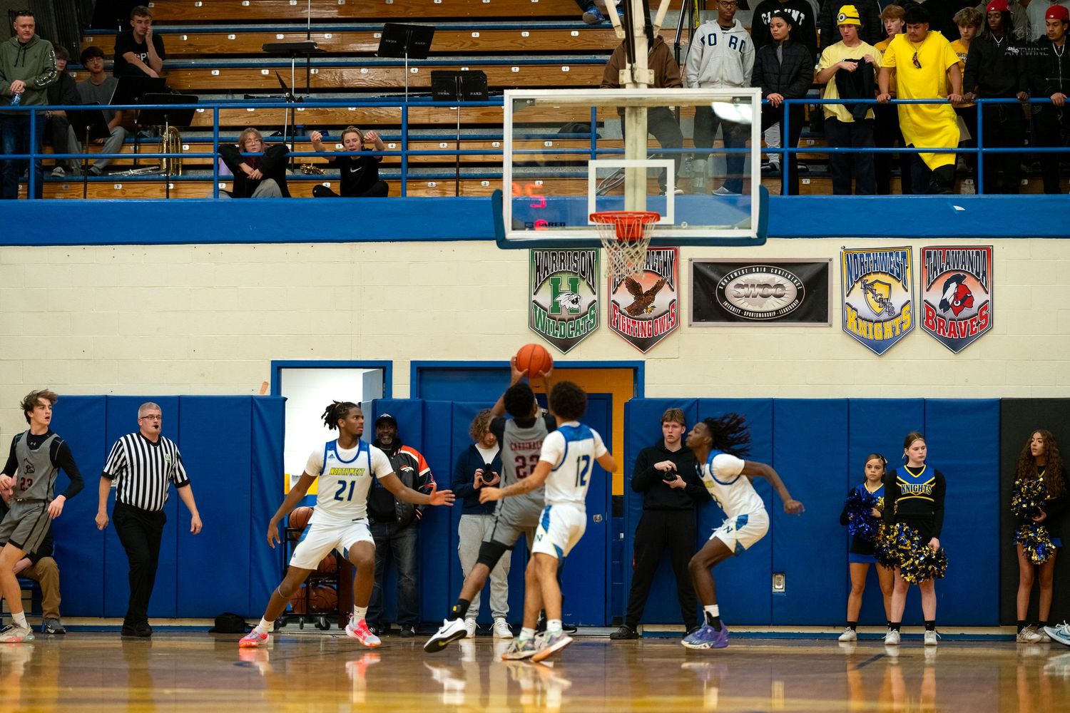 High school basketball players battle for loose ball during competitive indoor game with crowded sidelines.