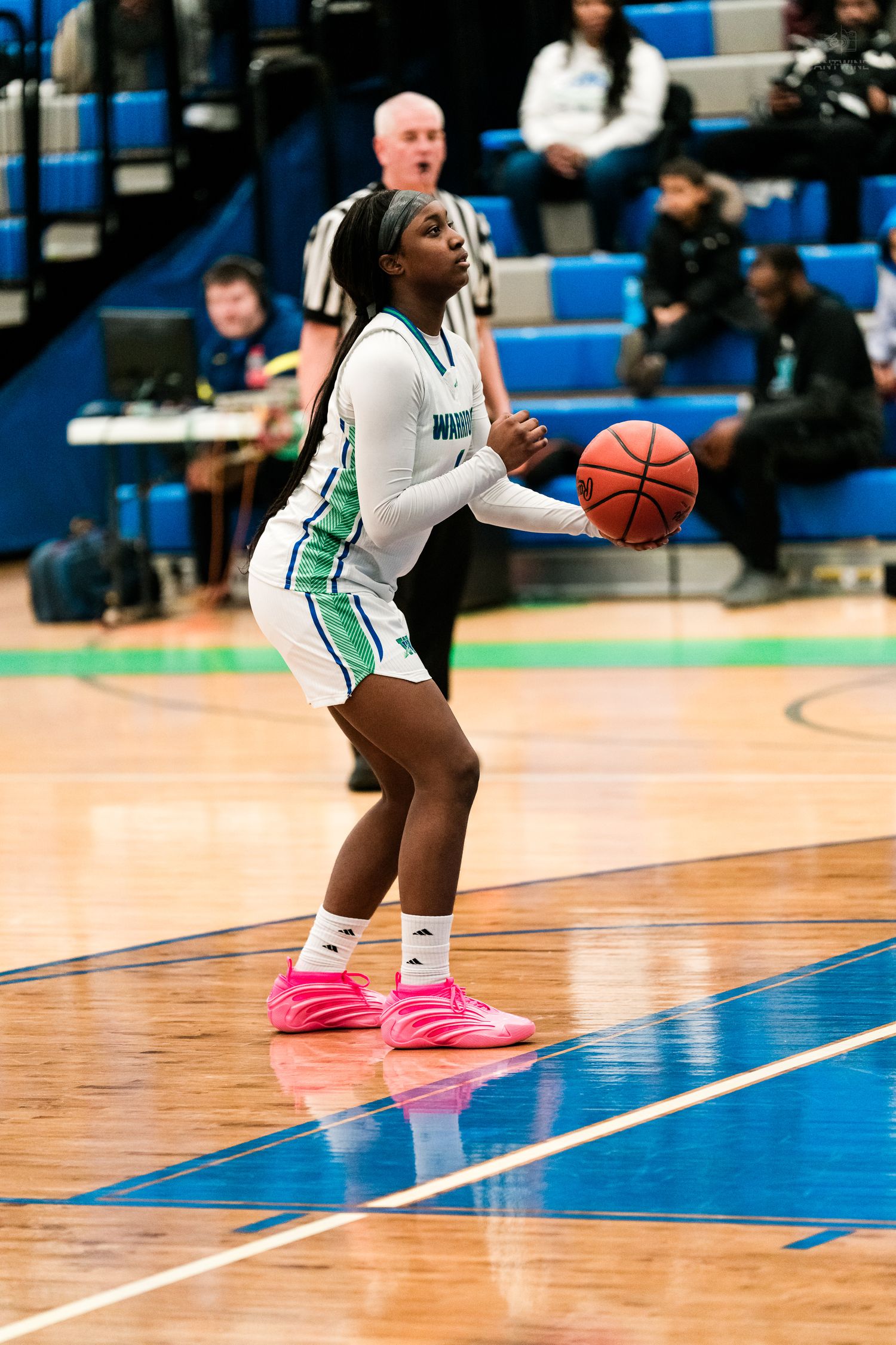 A female Warriors basketball player in white and green prepares to pass the ball while wearing pink sneakers on court.