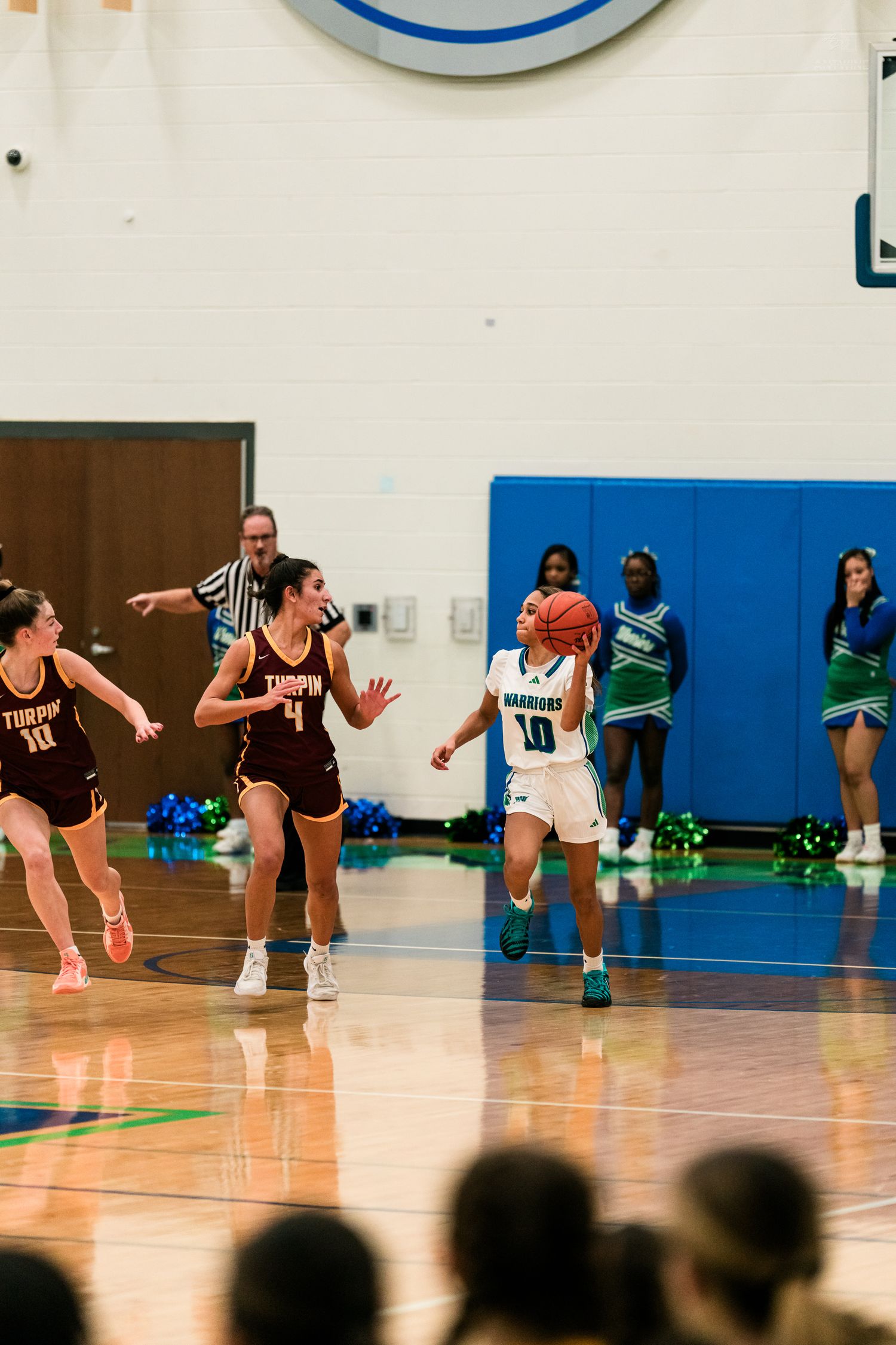 Warriors #10 prepares to shoot basketball while two Trojan defenders in maroon uniforms close in during game.