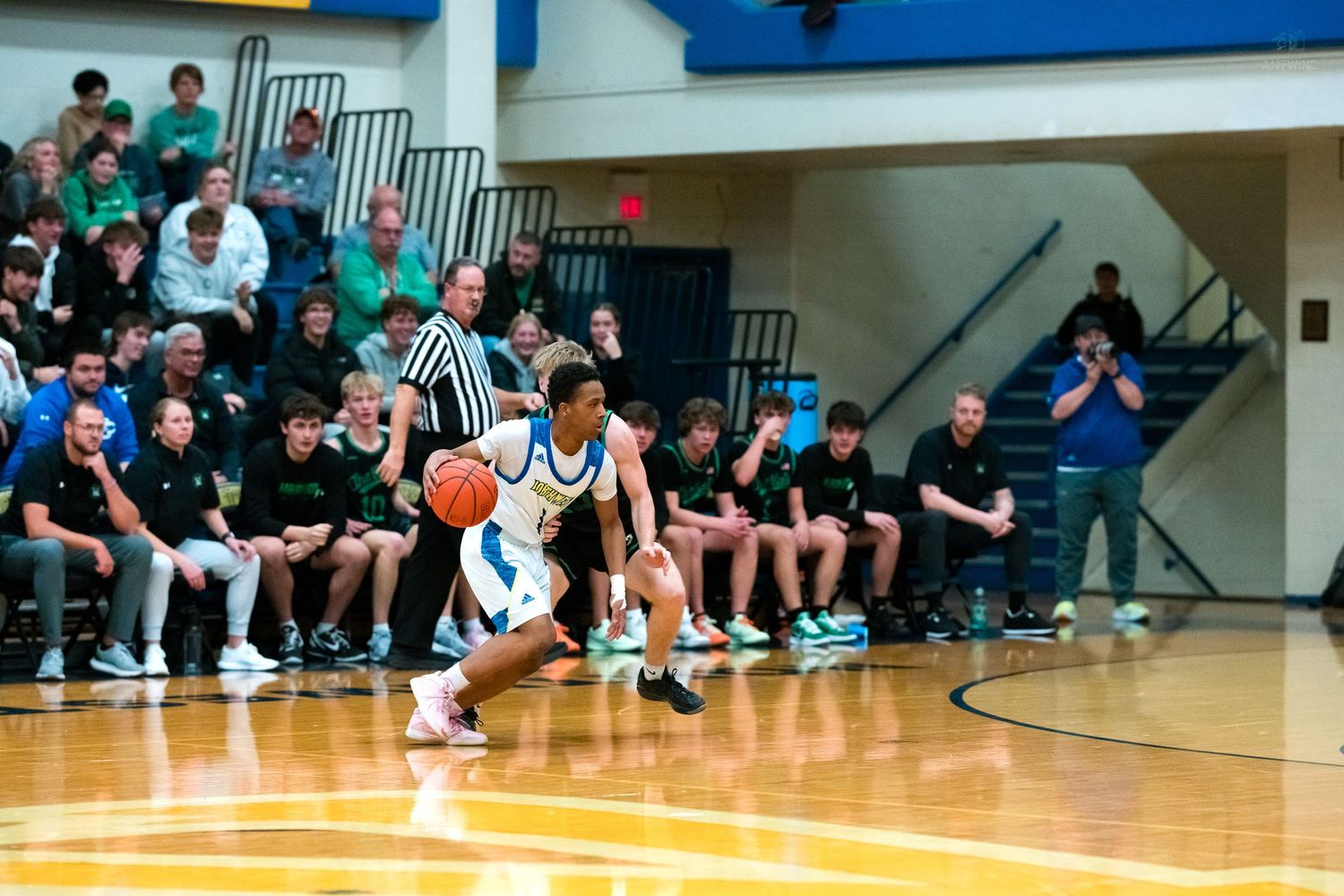 A high school basketball player in blue dribbles along the sideline with a crowd of spectators watching closely.