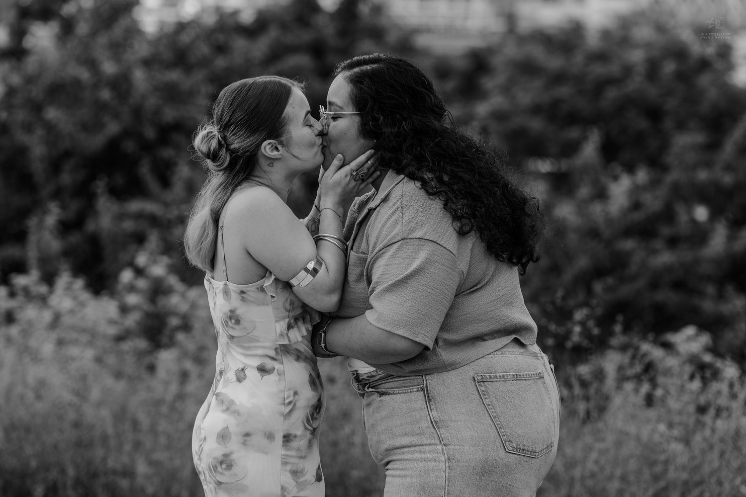 Two women sharing a romantic kiss outdoors in black and white photography.