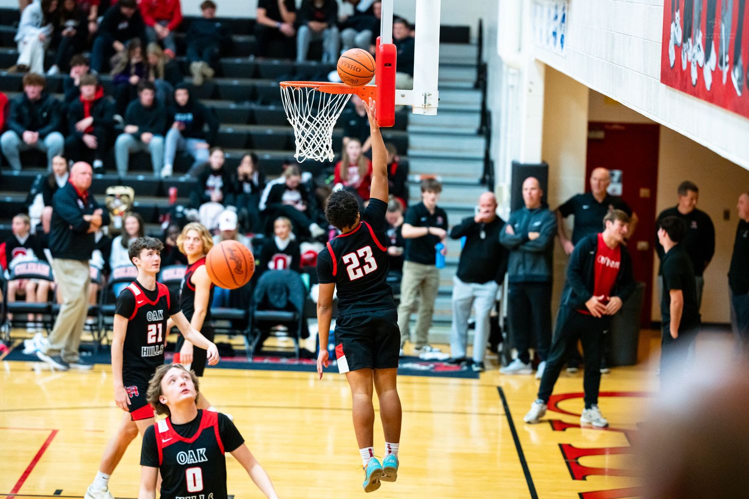 High school basketball player number 23 dunks the ball during a game with teammates watching below.