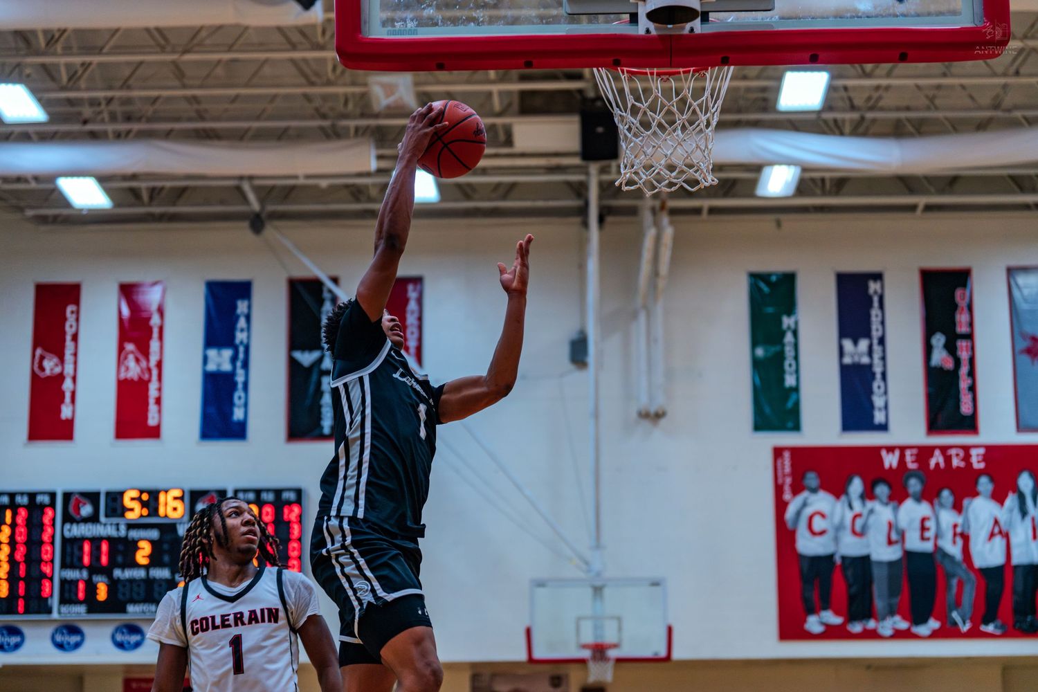Basketball player in black uniform attempts a slam dunk during a high school basketball game.