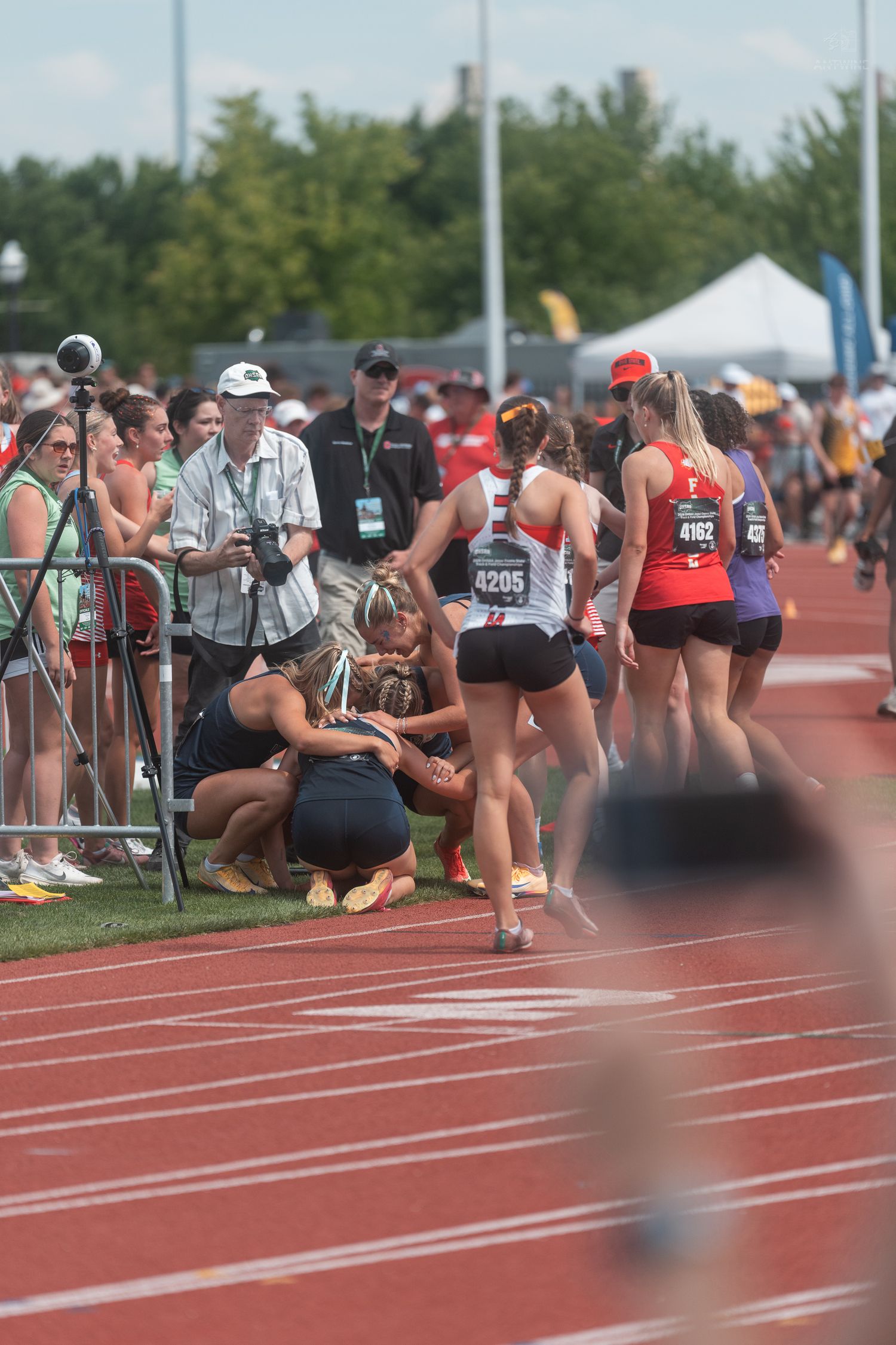 Female track athletes and spectators gather on the track after a relay race at an outdoor competition.