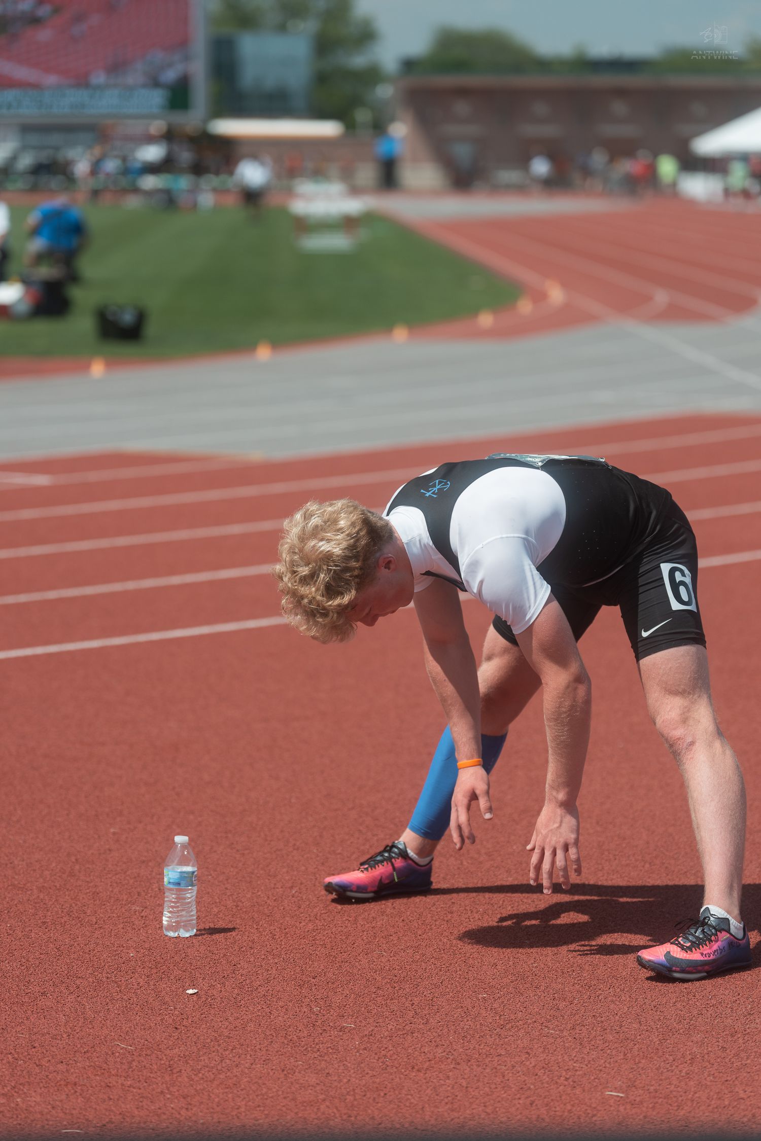 Exhausted male track runner number 6 bent over catching breath next to water bottle on red competition track.