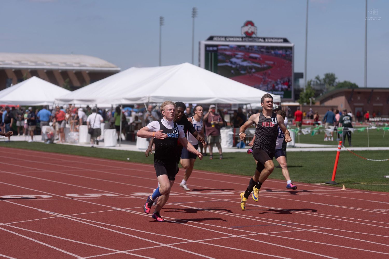 Two athletes sprint down the track during an outdoor track and field competition on a sunny day.
