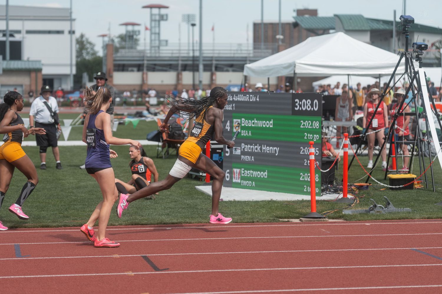 Male athlete runs past a scoreboard showing race times at the Ohio State Track and Field State Championship.