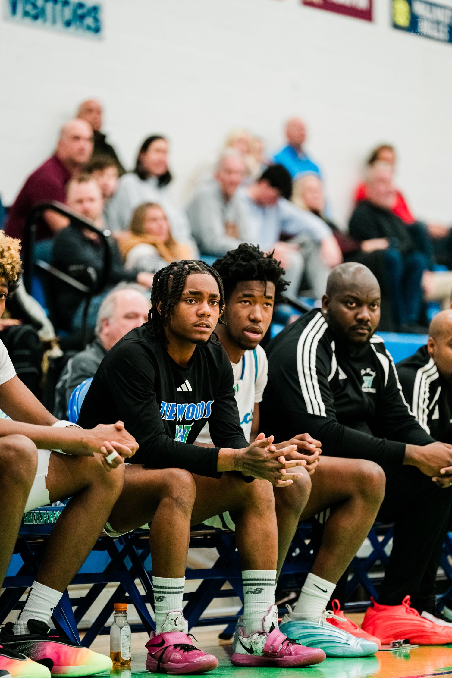 Lakewood Warriors players and coach sit attentively on the bench during a high school basketball game.