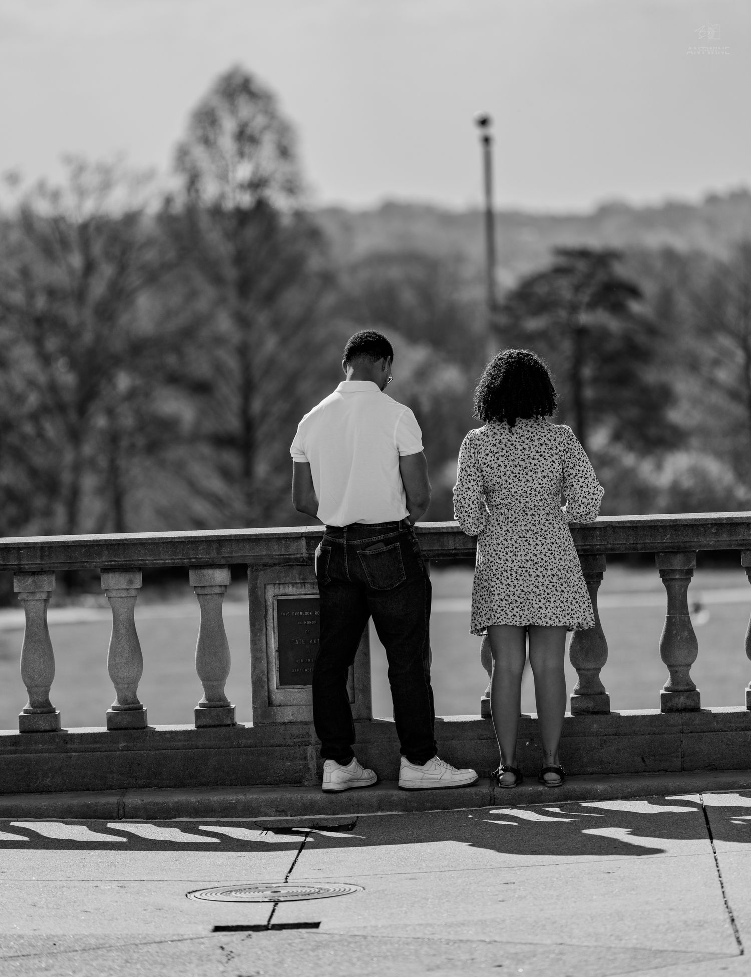 Black and white rear view of couple standing at classic stone balustrade in park.