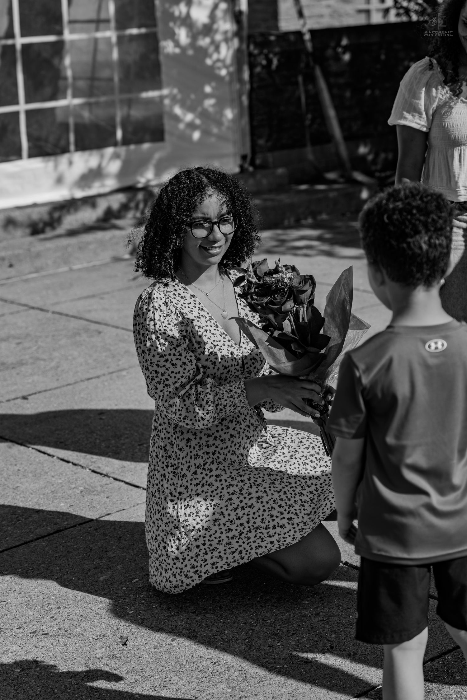 Young Black woman kneels to receive a bouquet of flowers from a young boy in black and white photo.