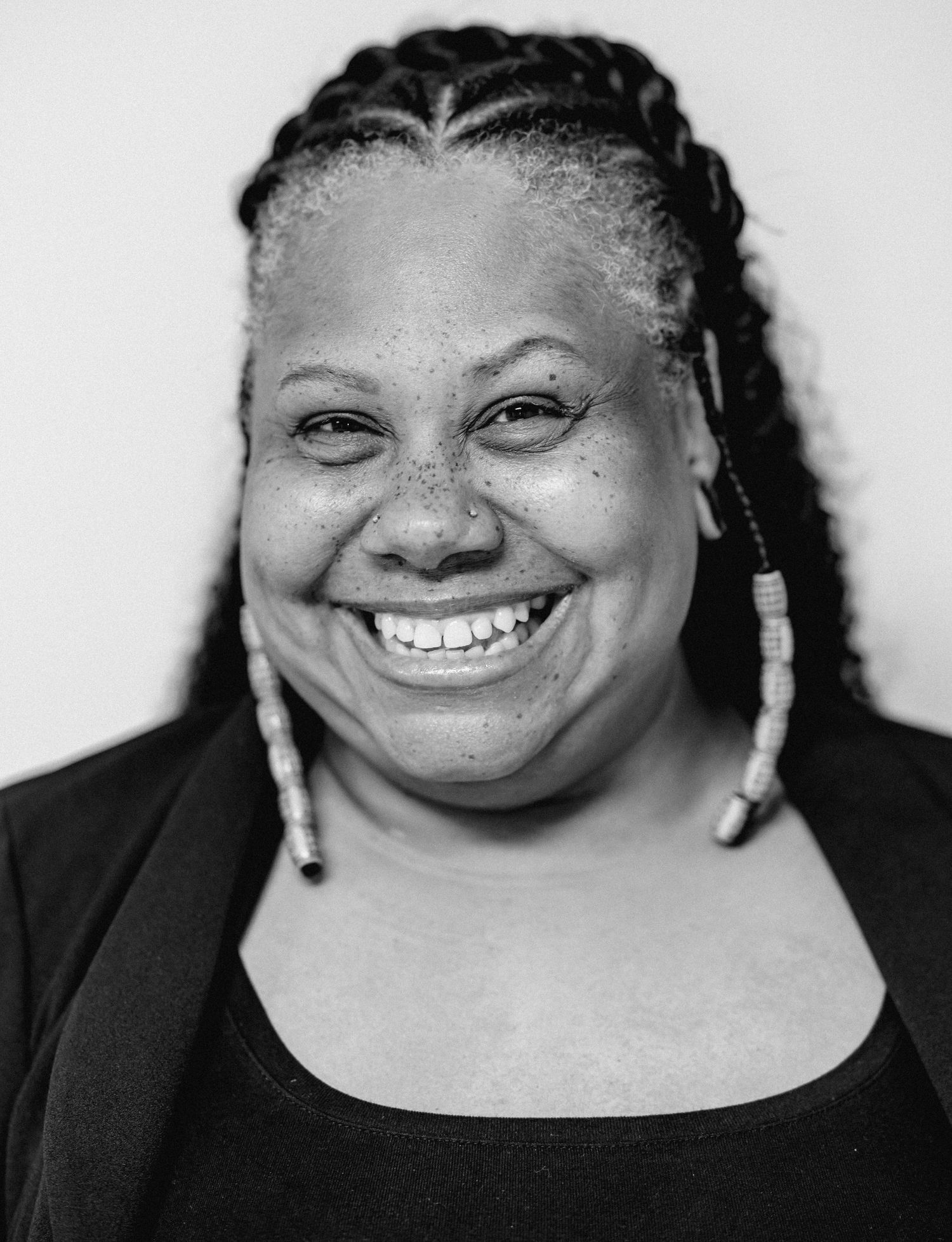 Smiling Black woman with braided hair and beaded earrings in black top, black and white close-up portrait.