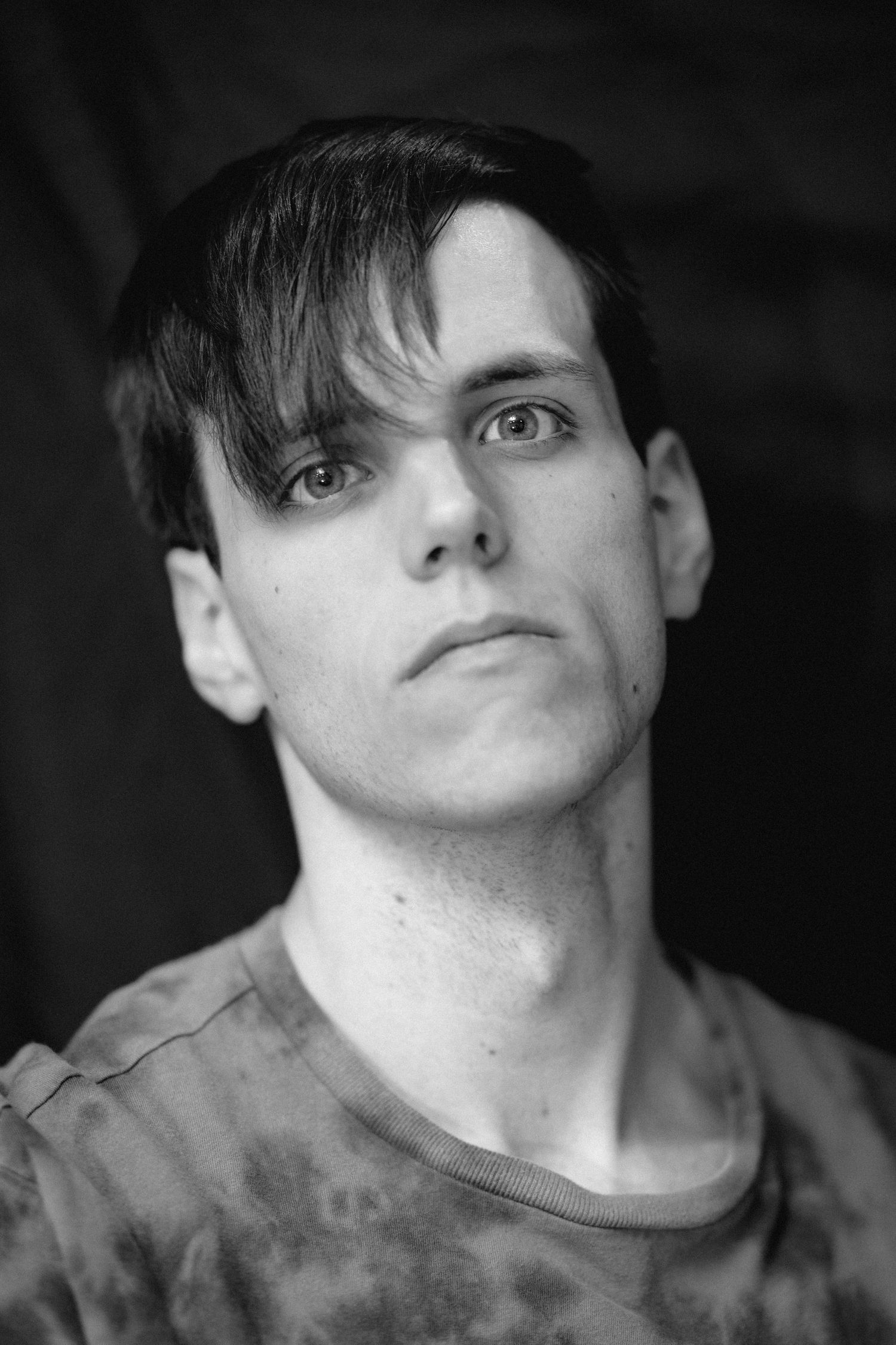 Black and white close-up of young man with dark bangs and intense expression.