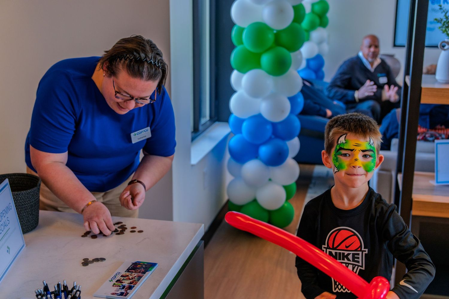 Staff member assists a child with face paint at a COPFCU grand opening celebration.
