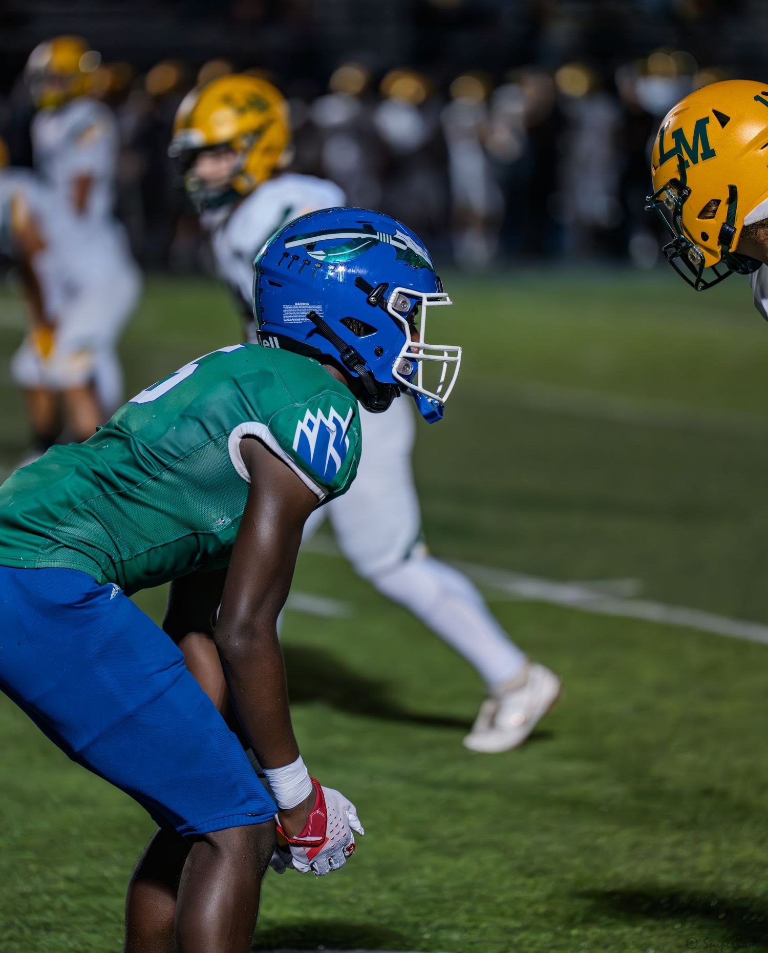 A Warriors defender in blue helmet faces off against a yellow-helmeted opponent at the line of scrimmage.