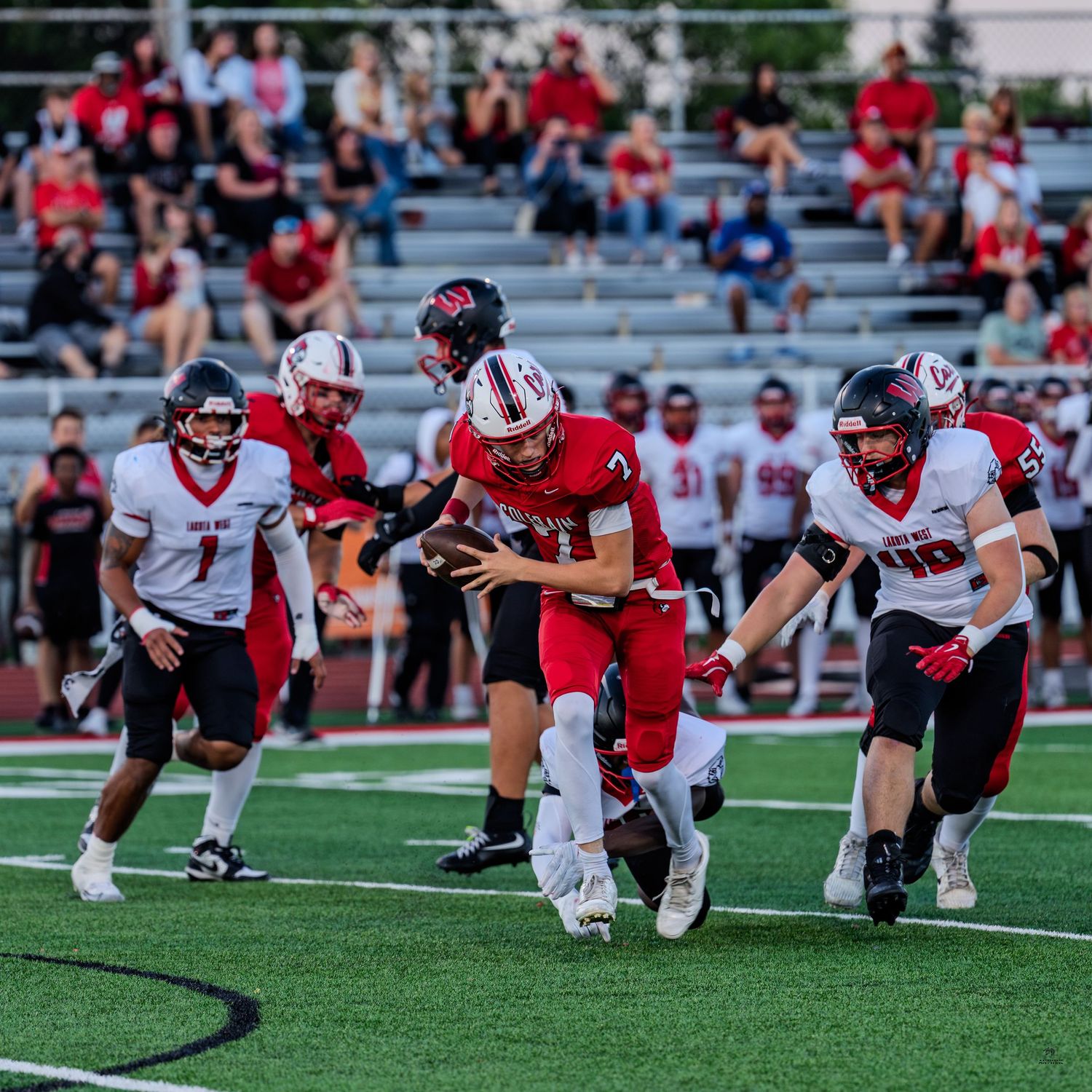 High school football ball carrier in red jersey breaks through defenders during an intense game play.