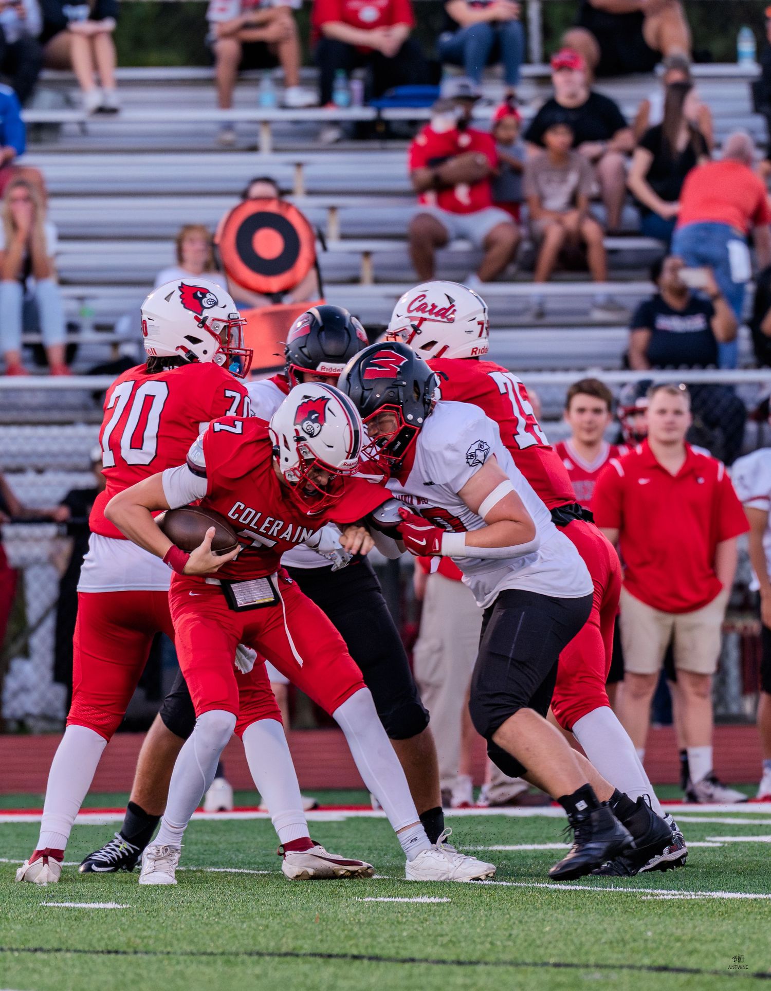 Colerain Cardinals quarterback pressured by defenders during competitive high school football game action.
