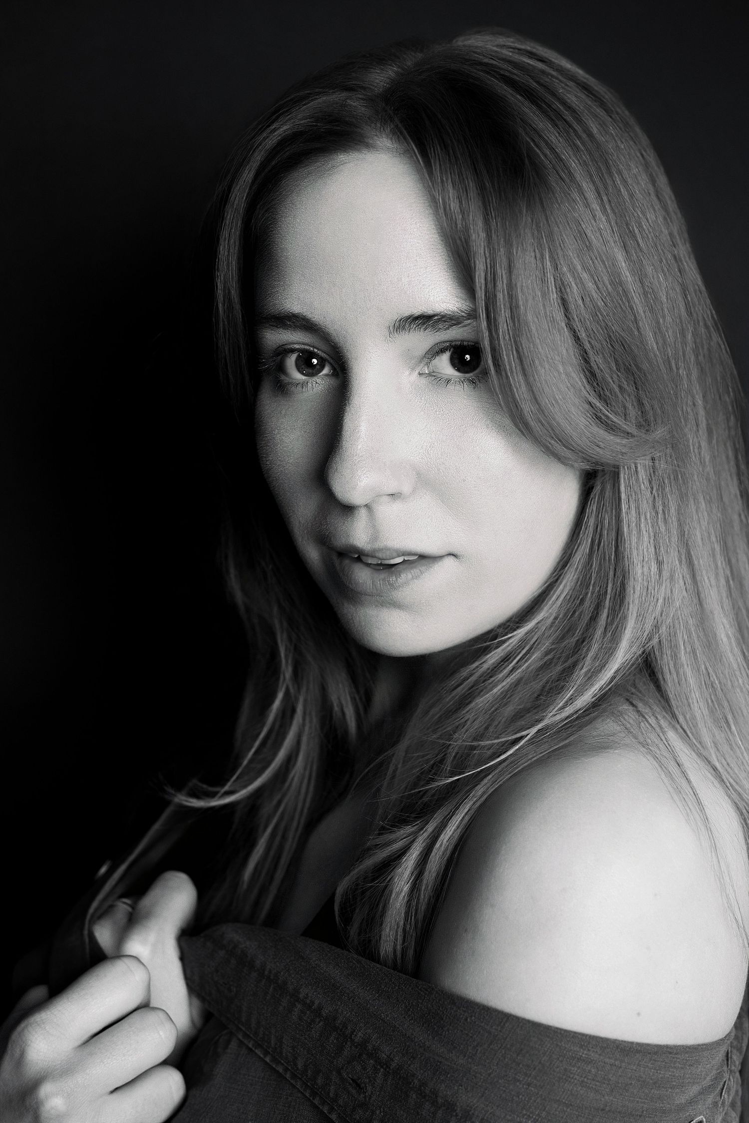 Black and white portrait of young woman with long hair in off-shoulder top against dark background.