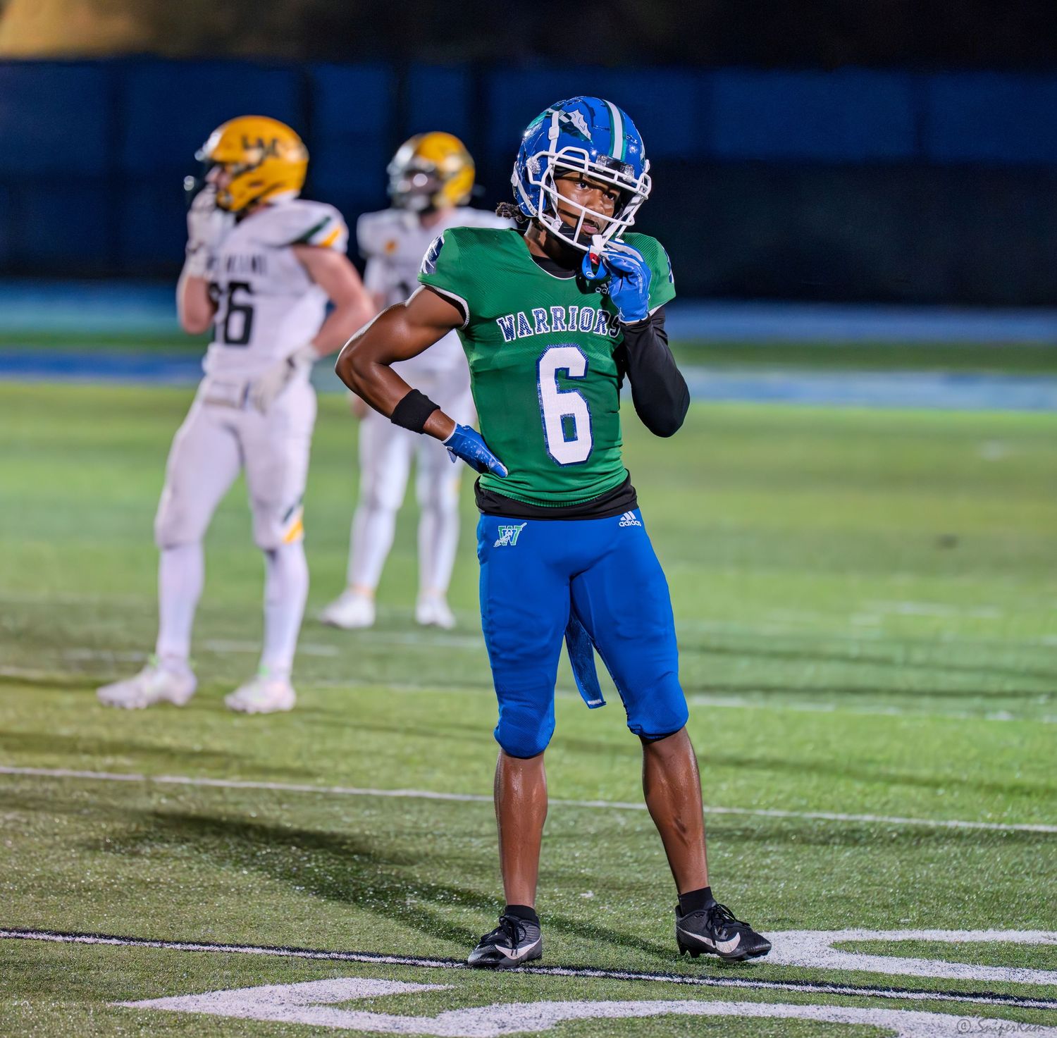 Football player #6 in green and blue Warriors uniform celebrates on the field during a night game.