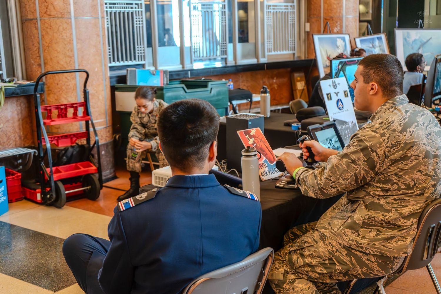 Two military personnel in uniform collaborate on a tablet at an indoor event.