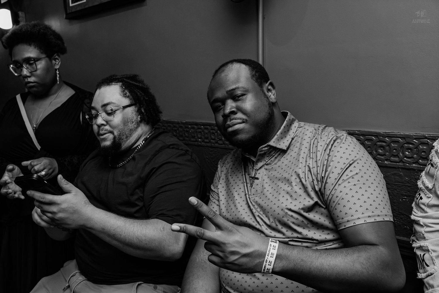 Black and white photo of three people sitting together, two men looking at a phone in a dimly lit room.