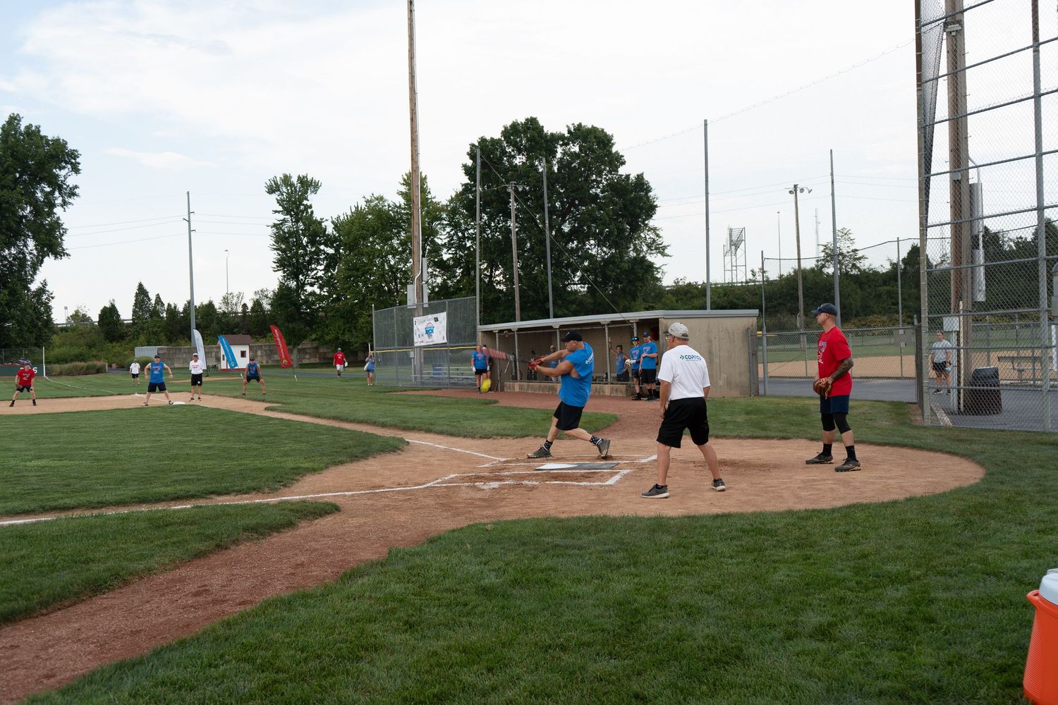 Group of adults playing recreational softball on a baseball diamond during an evening outdoor game.