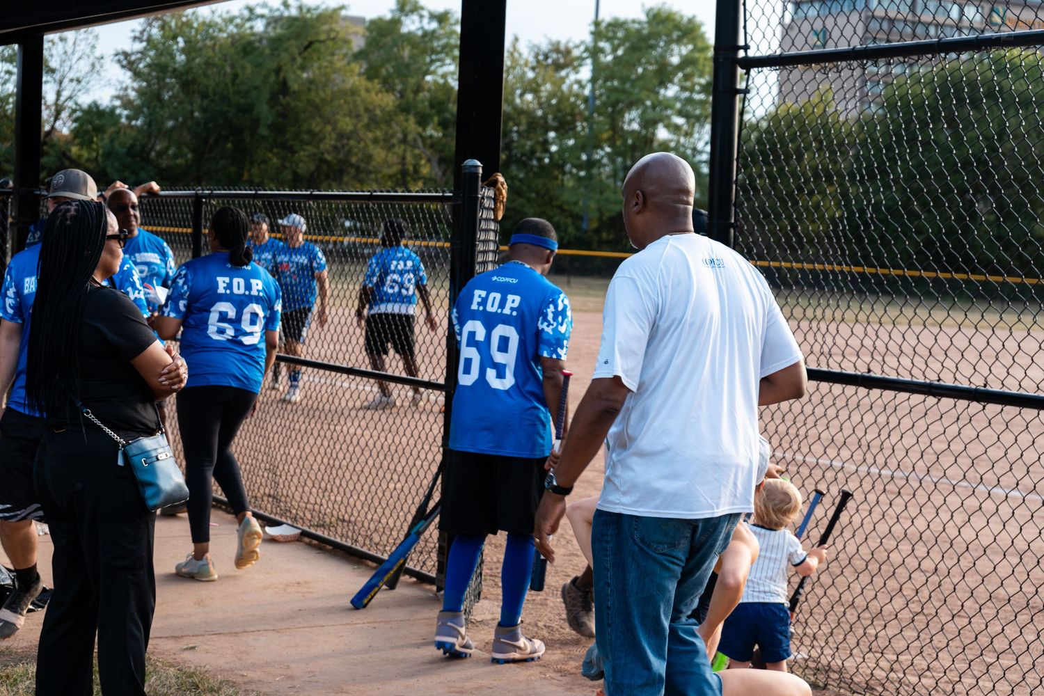 Youth baseball team in blue number 69 jerseys walking along dugout fence during a game.