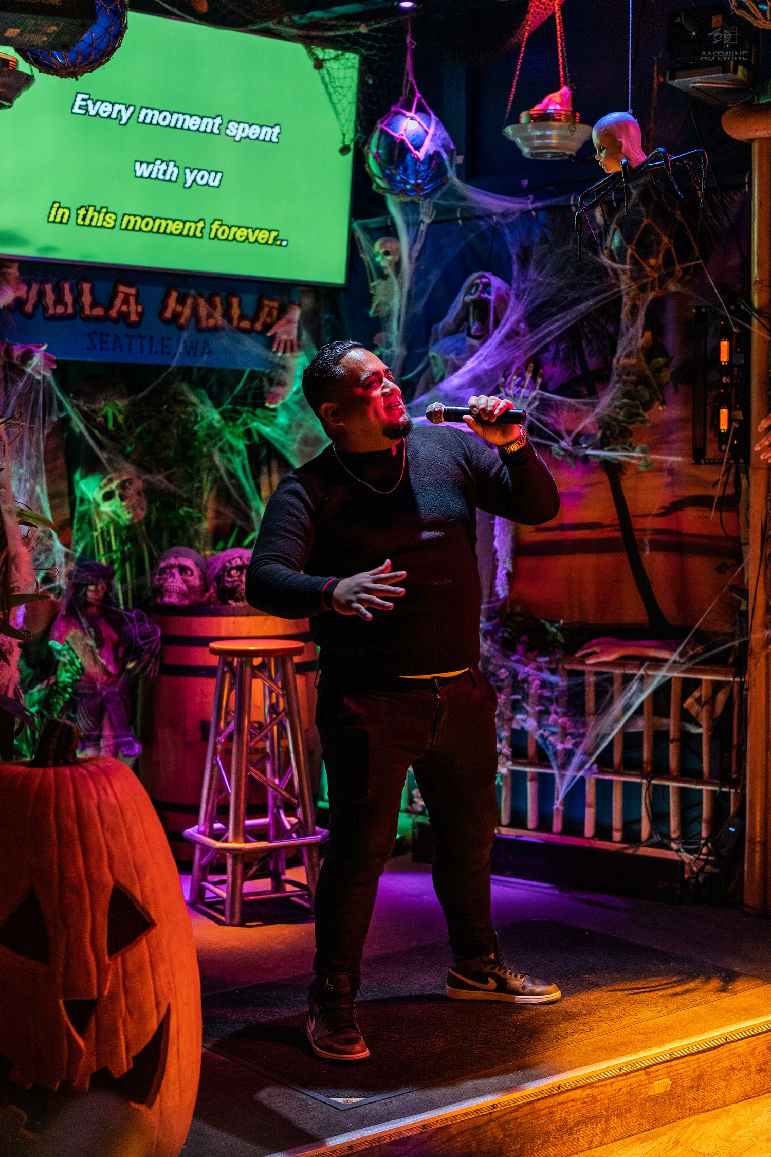 Male singer performing karaoke on colorful Halloween-decorated stage with jack-o-lantern at Hula Hula.