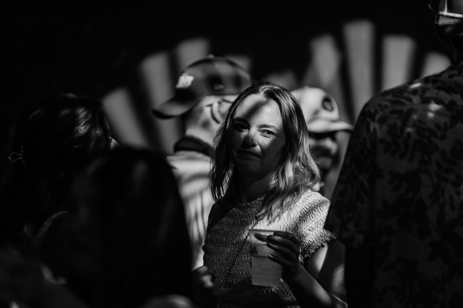 Black and white photo of a woman wearing a face mask at a crowded event, holding a drink.