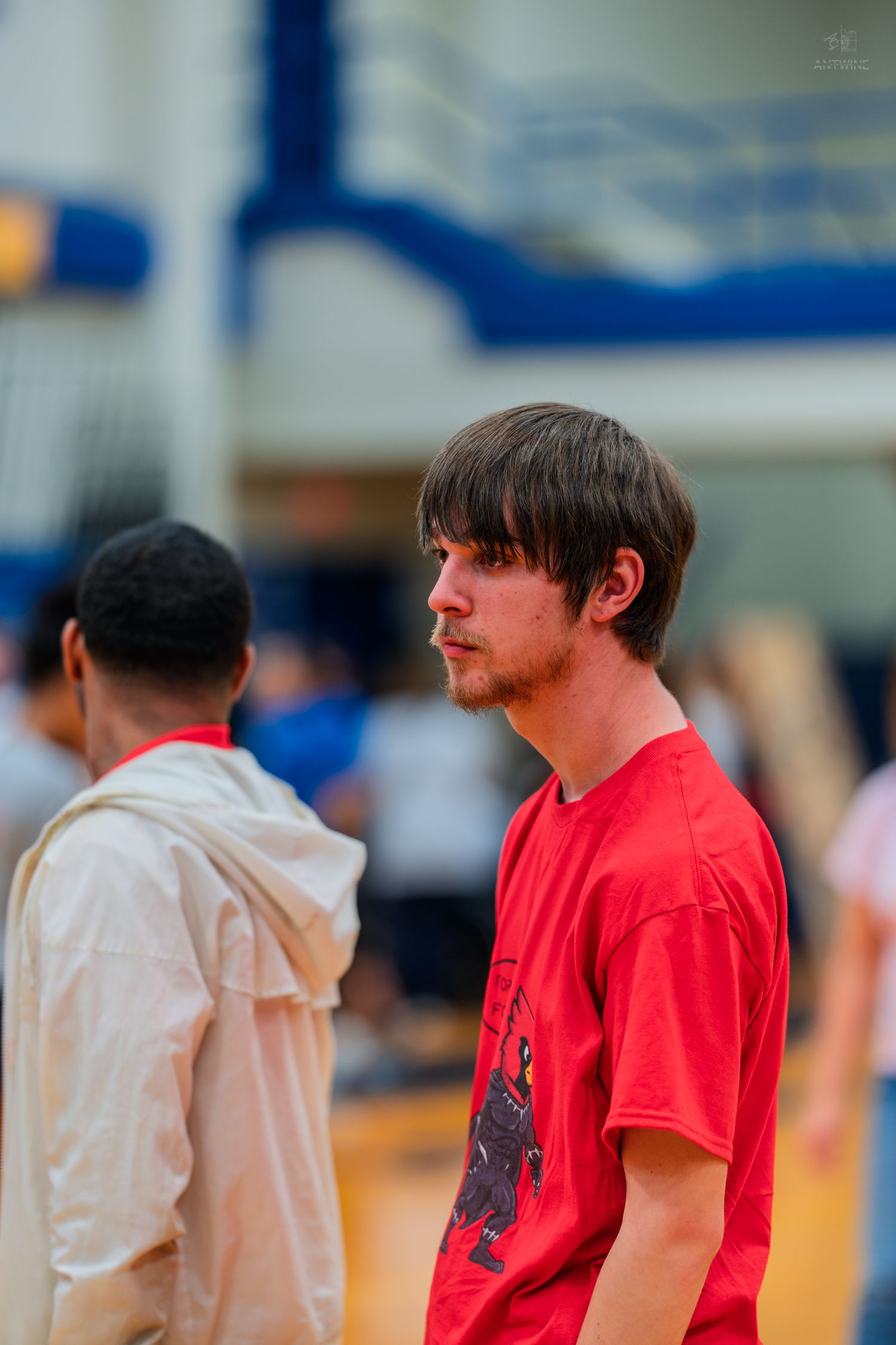 Young man in red t-shirt standing on a basketball court gymnasium floor during a game or practice.