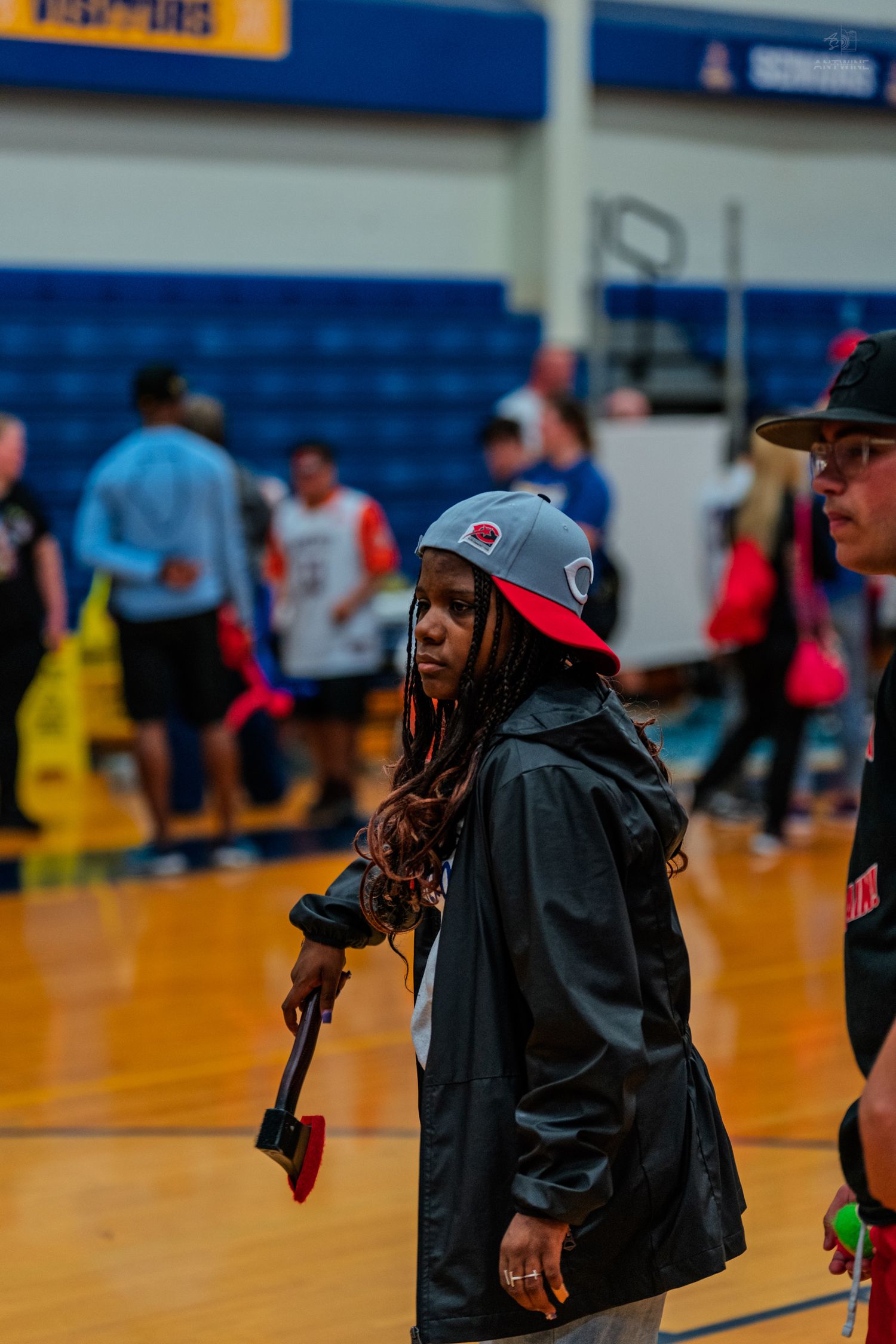 Woman in gray snapback cap and black jacket stands on basketball court during a game event.