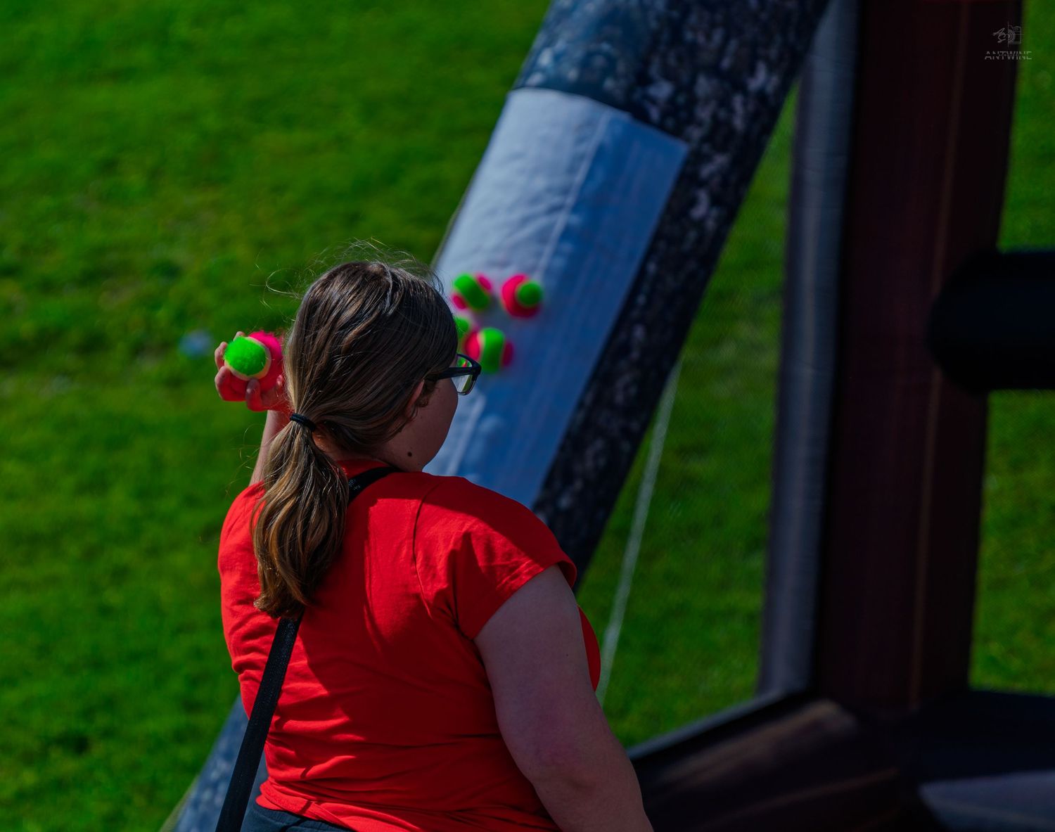 Woman in red shirt tossing colorful balls into an inflatable game at an outdoor event.